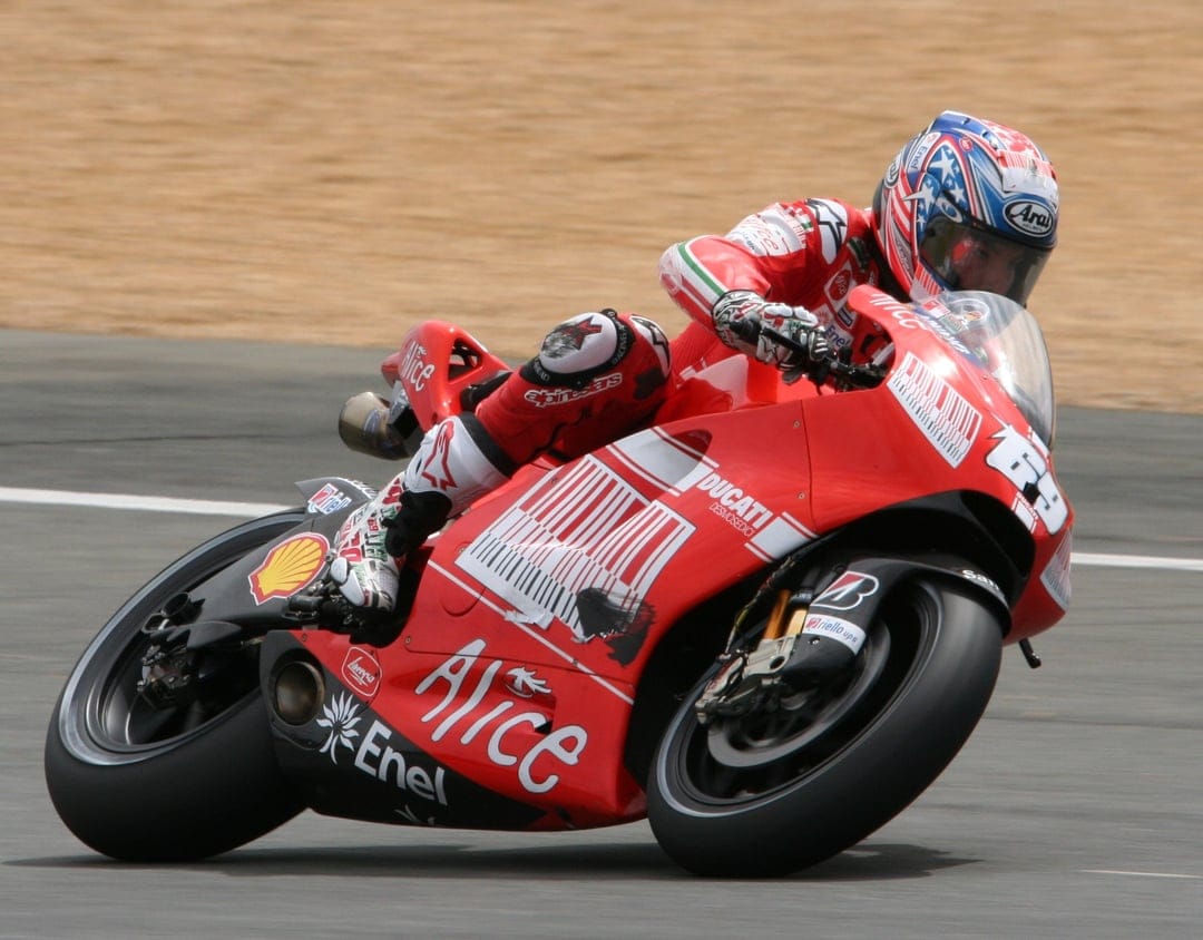 Professional motorcycle racer on a red Ducati leans into a racetrack corner during a high-speed sports event.