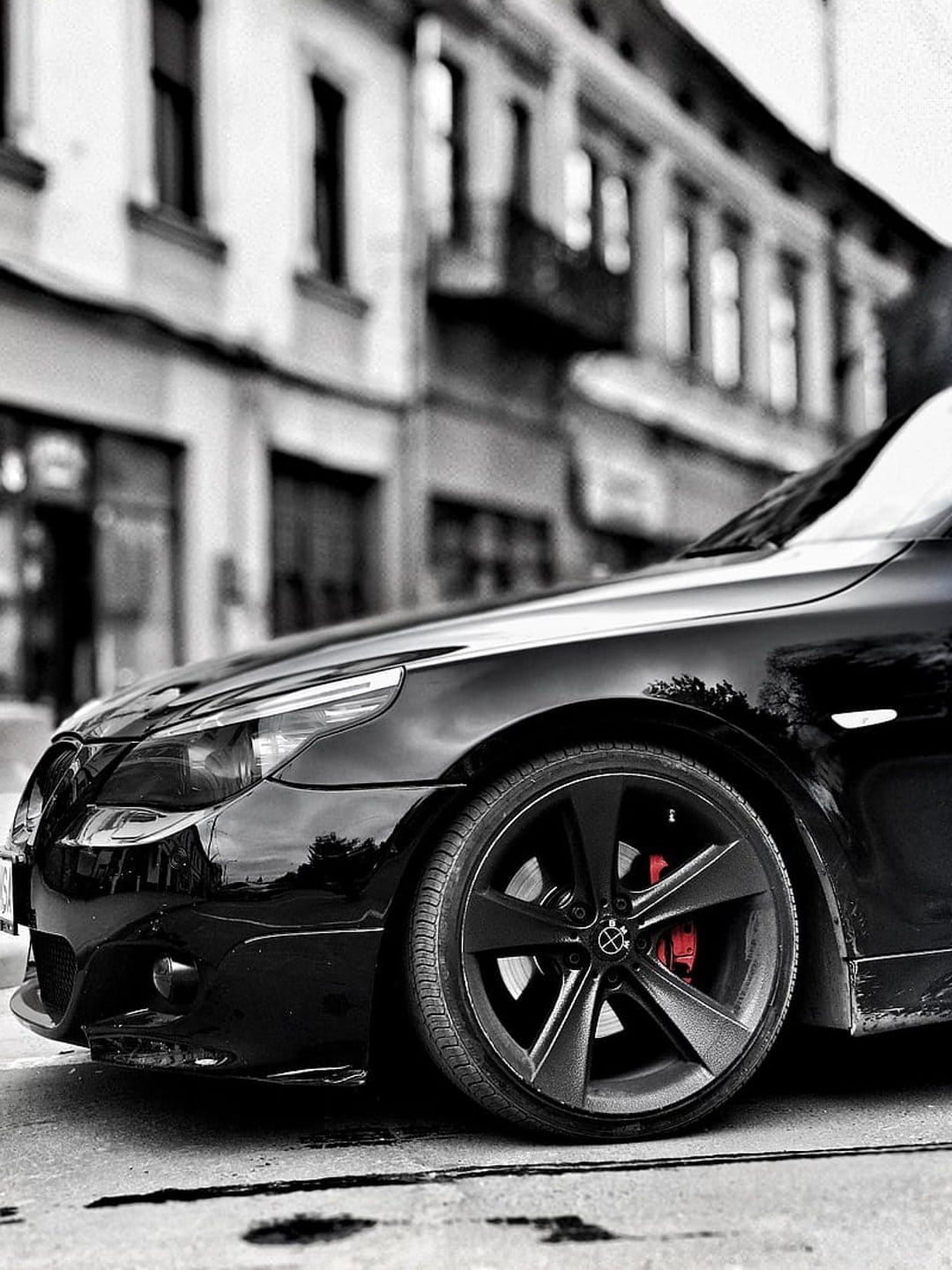 BMW alloy wheel with a bright red brake caliper parked on a city street with a blurred urban background.