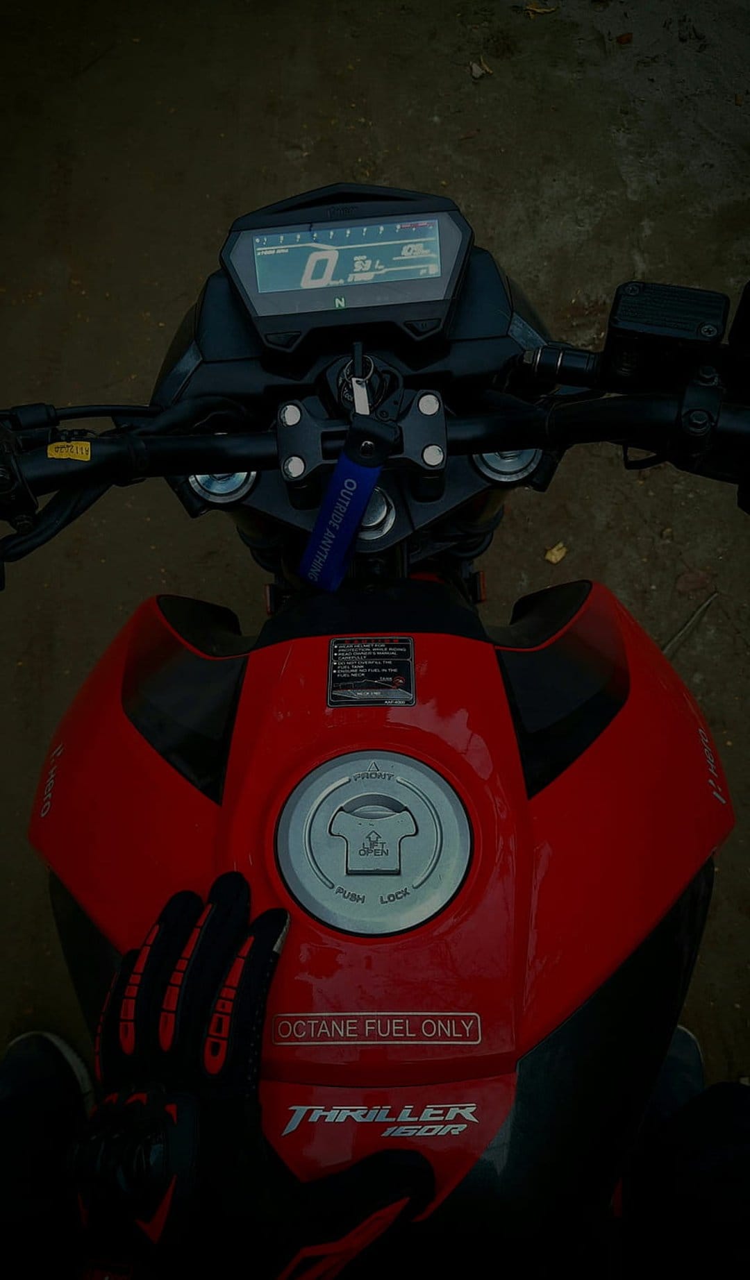 Rider's hands in red and black gloves grip the handlebars of a red motorcycle with a digital dashboard display.