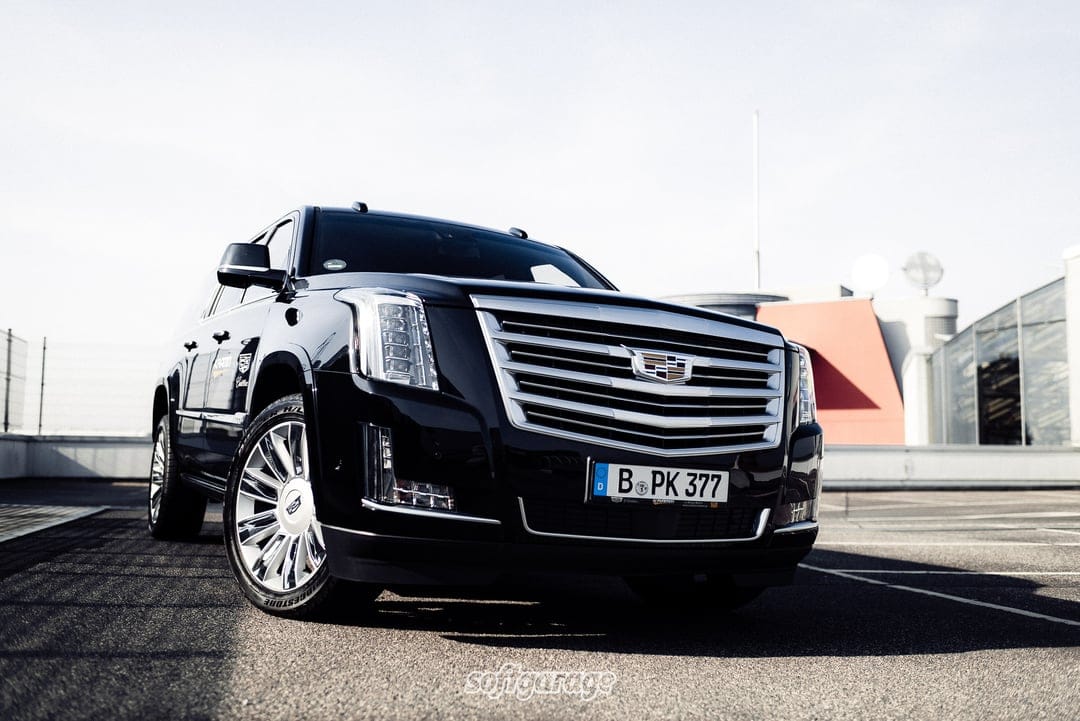 Black Cadillac Escalade luxury SUV with chrome accents parked on an open asphalt lot during a bright sunny day.