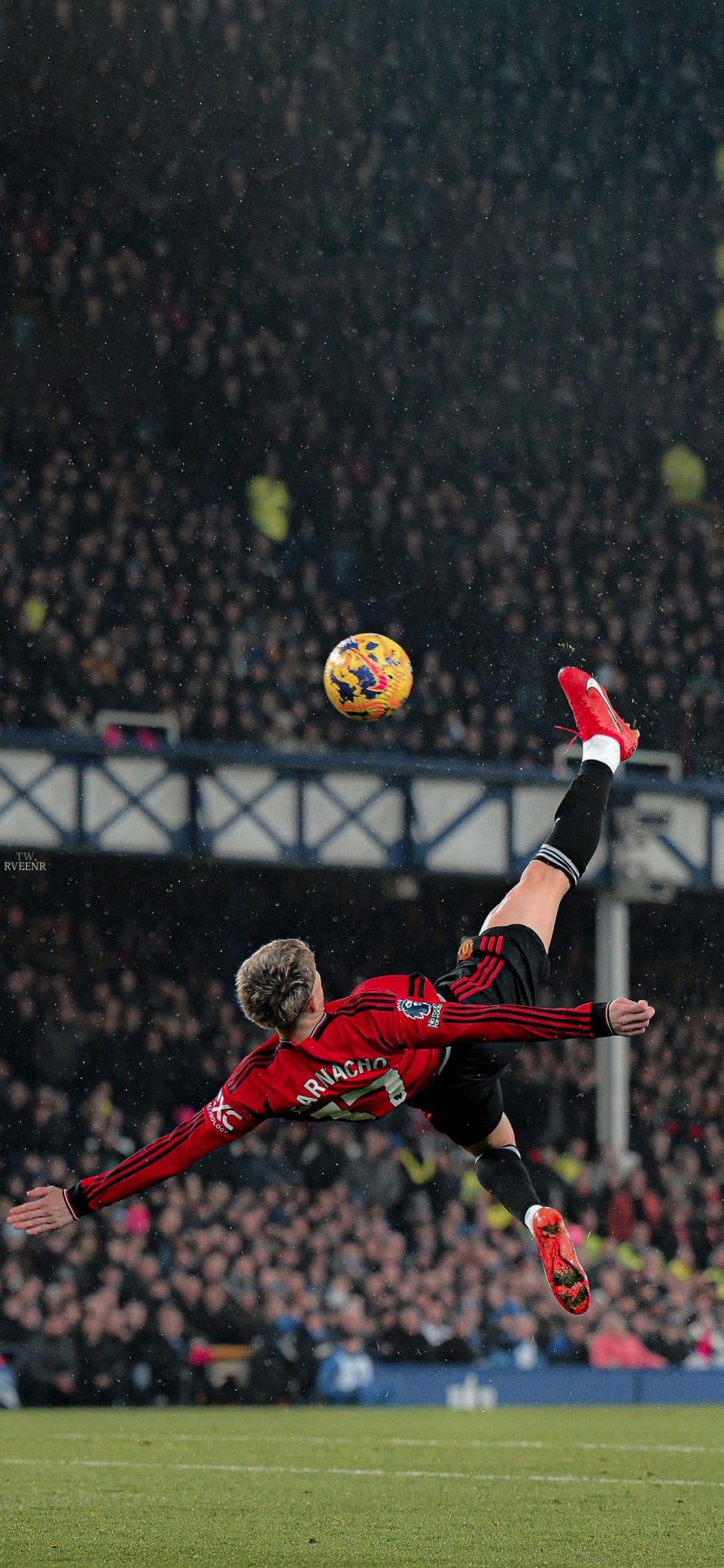 Professional footballer performs a bicycle kick mid-air in a crowded stadium for a vertical phone screen.