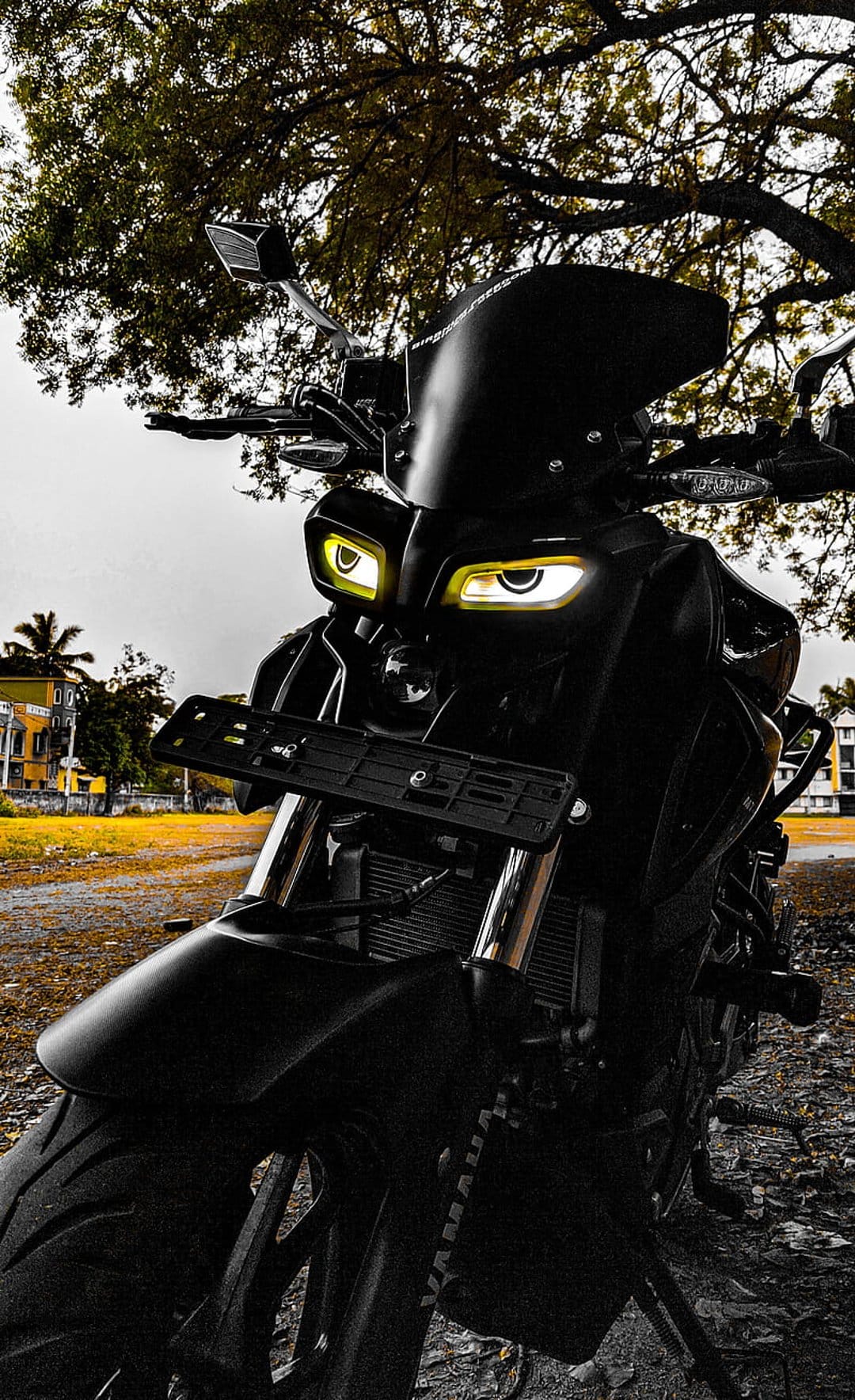 Black Yamaha motorcycle with circular yellow glowing headlights parked outdoors near a tree and building.