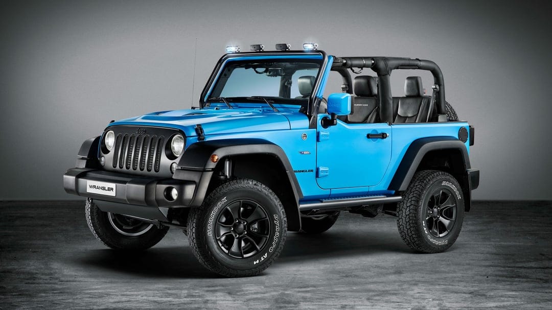 Blue Jeep Wrangler Rubicon with top off, black roll cage, and roof lights on a neutral gray studio background.