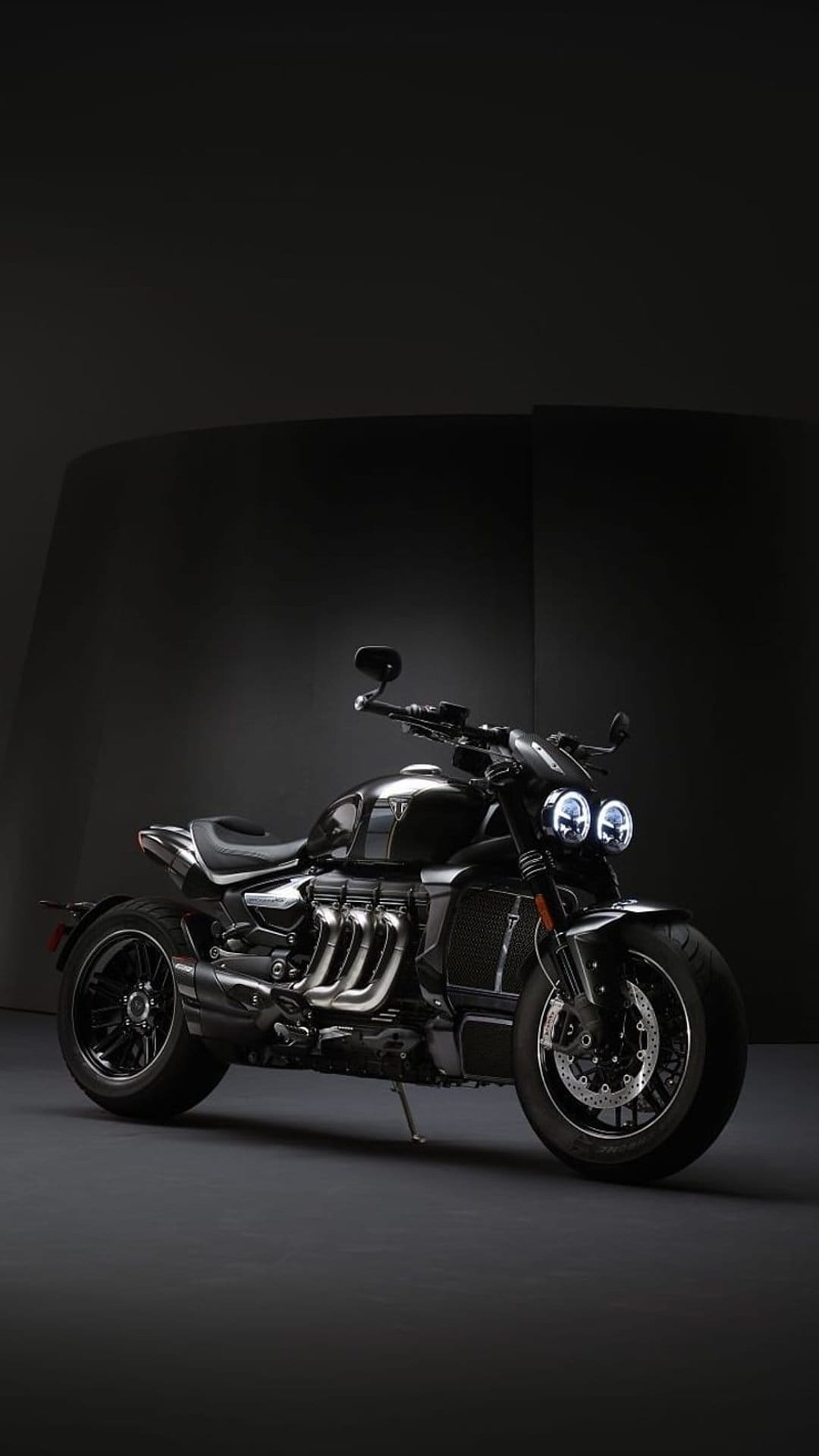 Triumph Rocket 3 motorcycle in a dark studio with dramatic rim lighting on its black frame and triple exhausts.