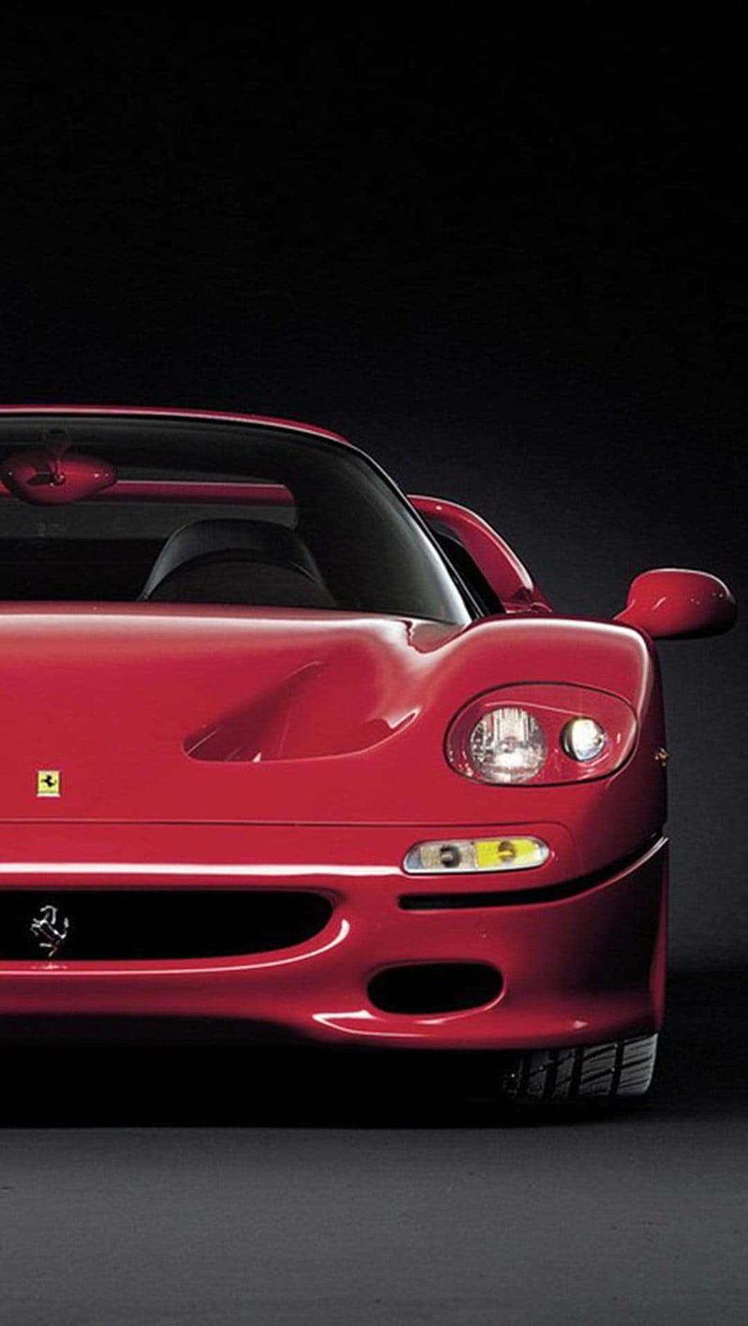 Ferrari F50 front end featuring red paint, a yellow emblem, and sleek headlights against a dark background.