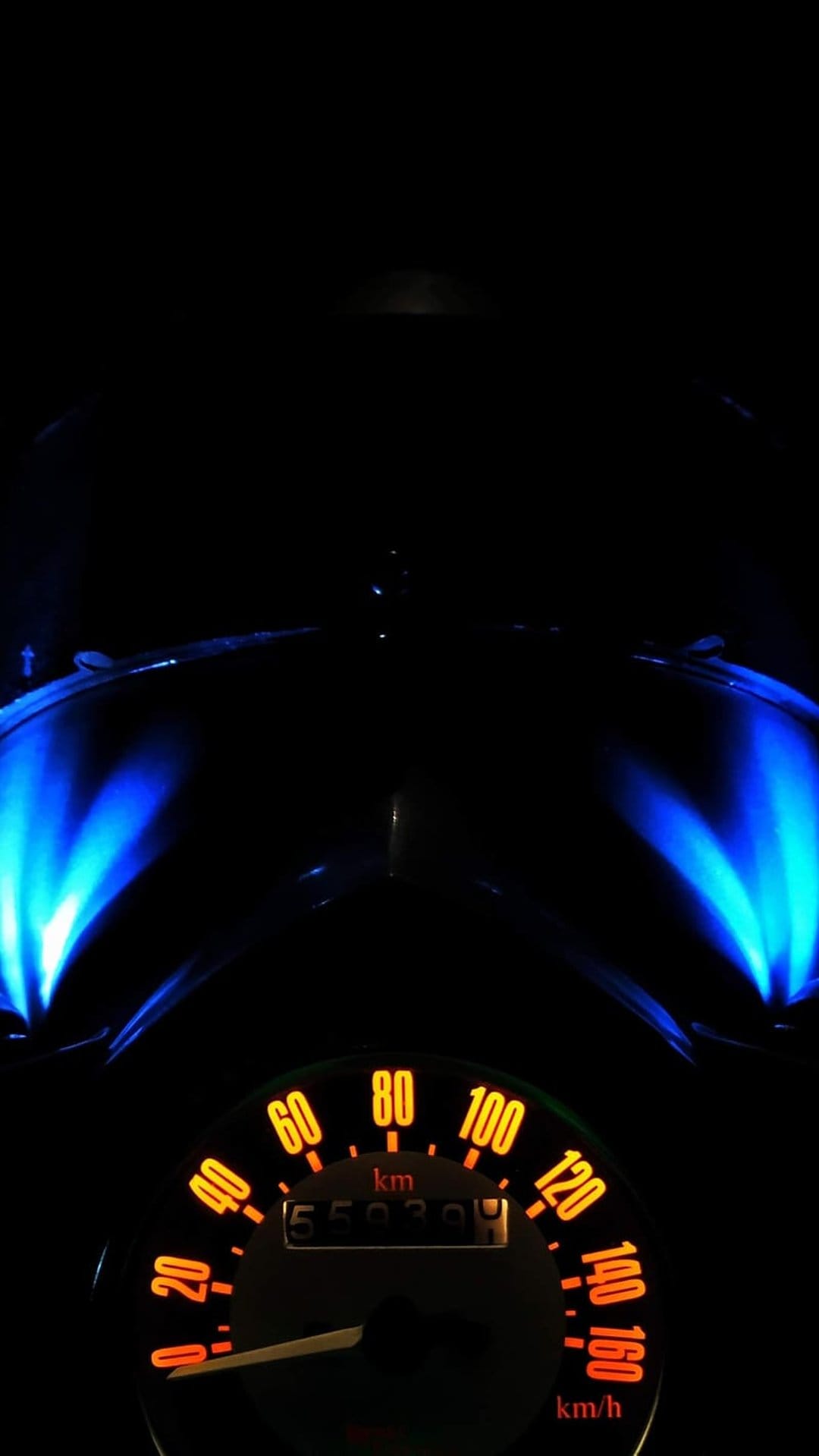 Motorcycle speedometer with orange numbers and a white needle glows beside vibrant blue fairing lights at night.