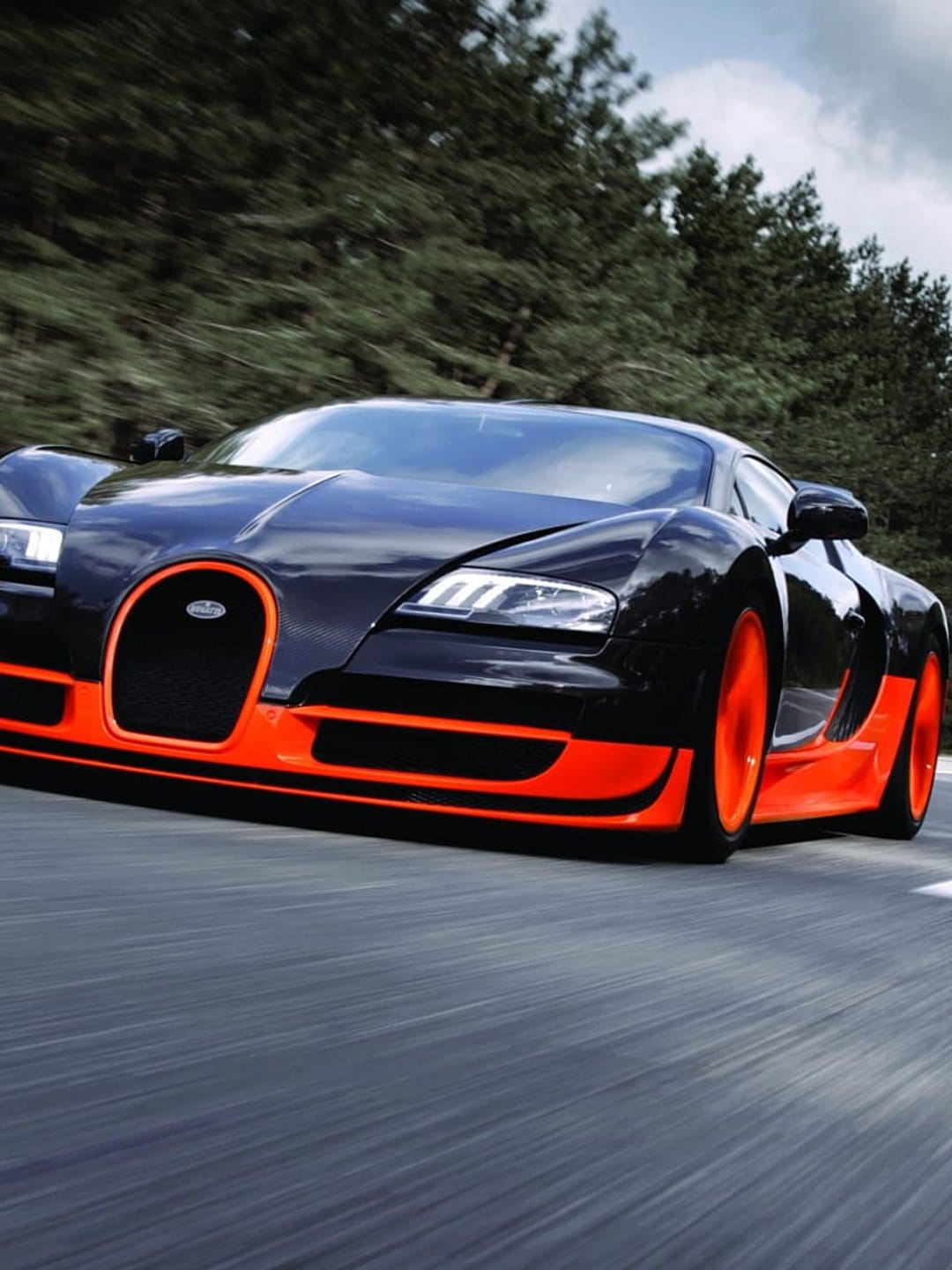 Bugatti Veyron with orange accents speeds down a forest road with heavy motion blur on the surrounding trees.