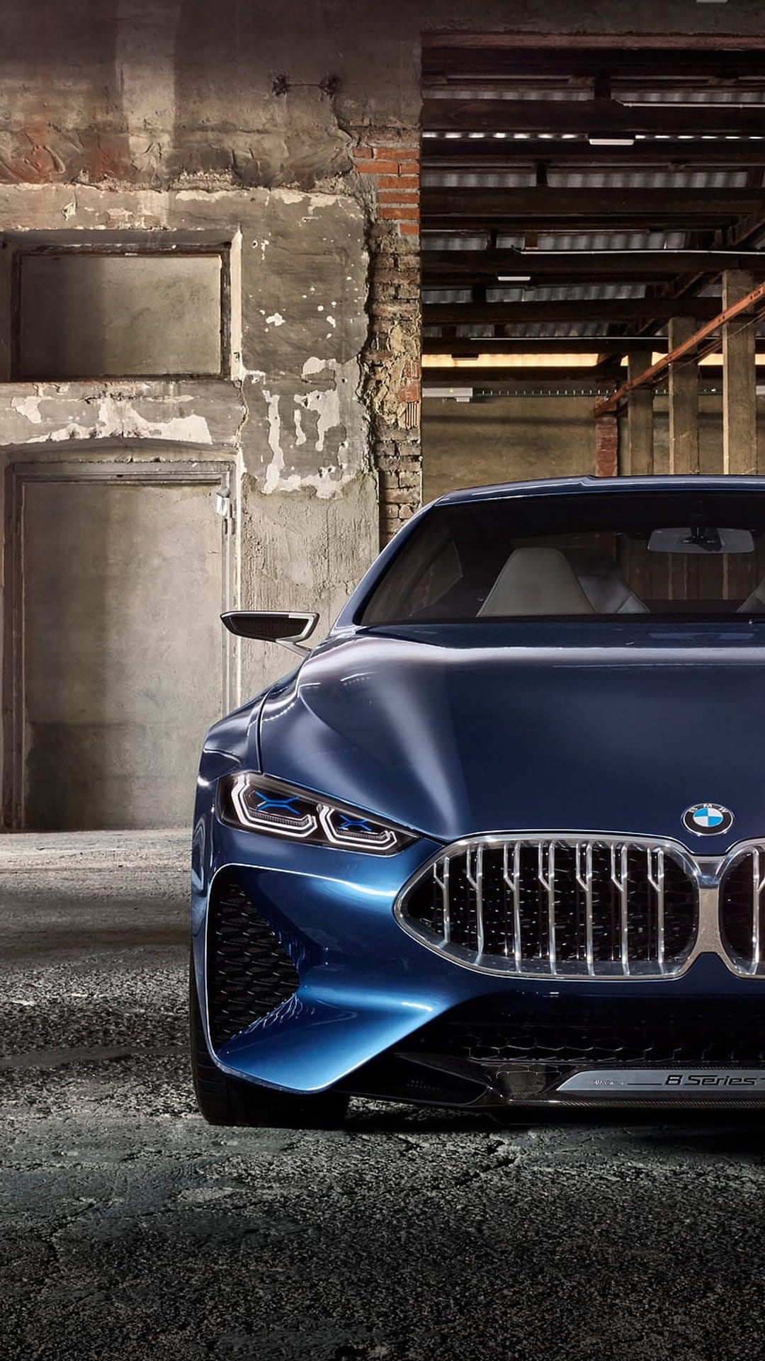 Blue BMW 8 Series concept car with sleek LED headlights parked against a weathered concrete and brick wall.