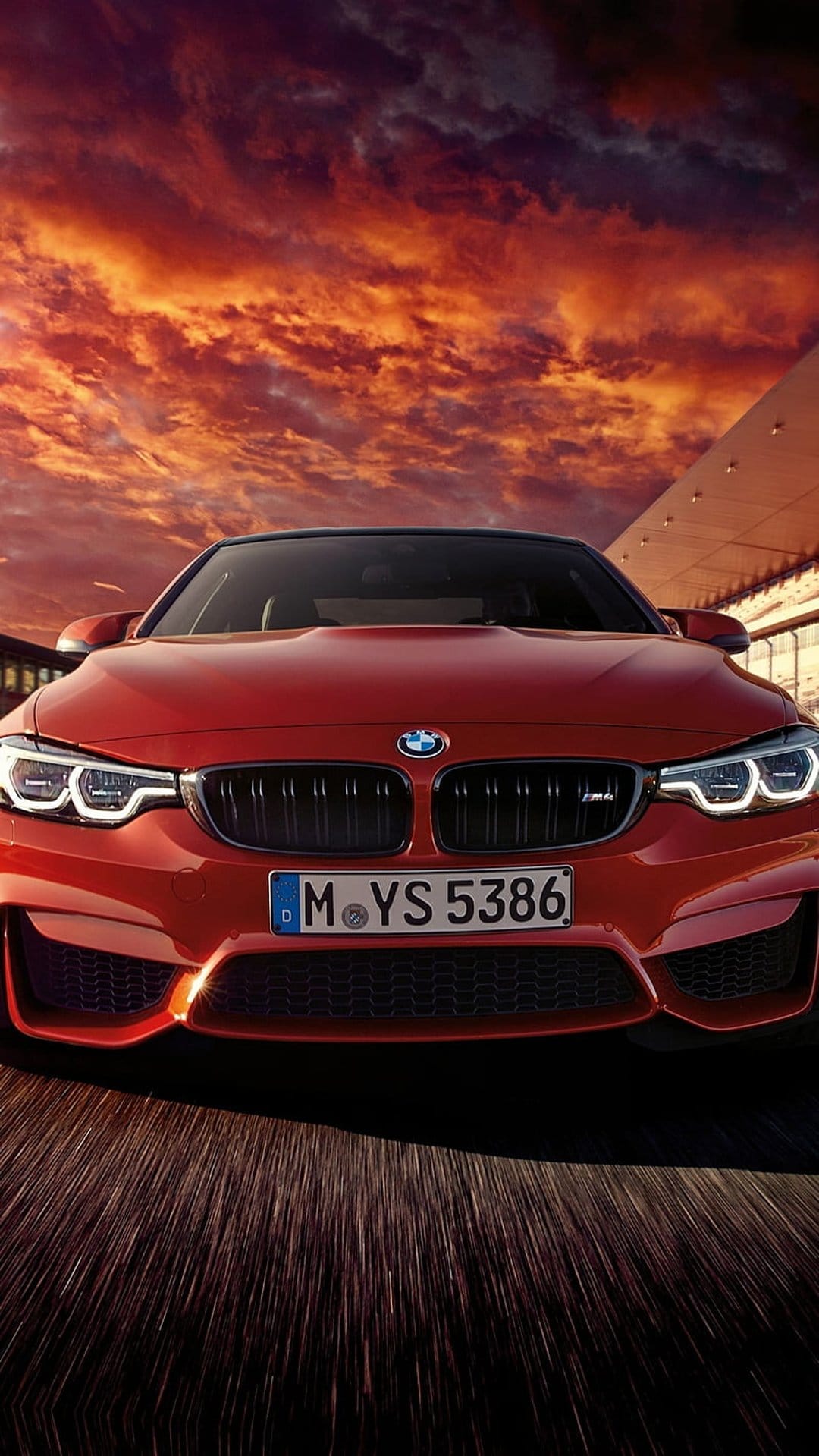 Red BMW M4 convertible parked on a road against a dramatic orange and red sunset sky with golden hour lighting.