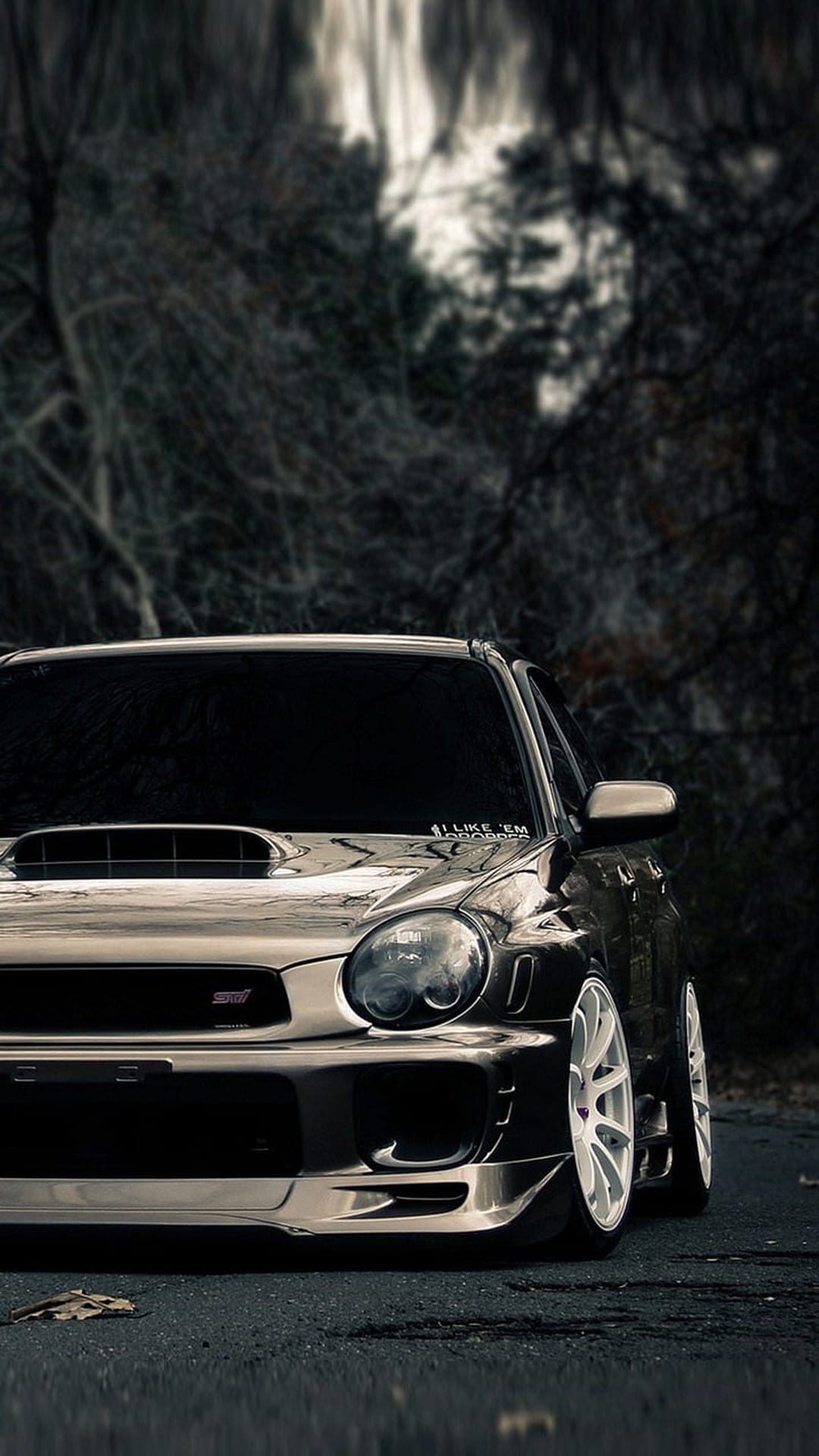 Subaru WRX STI featuring white rims parked on a wet forest road under soft, ethereal light filtering through trees.