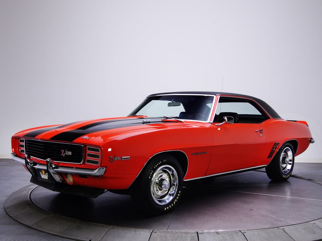 Orange 1969 Camaro Z28 with black racing stripes and vinyl top on a studio turntable with soft overhead lighting.