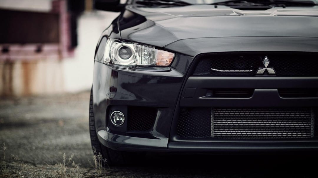 Close-up of a dark grey Mitsubishi Lancer headlight, mesh grille, and intercooler in soft lighting.