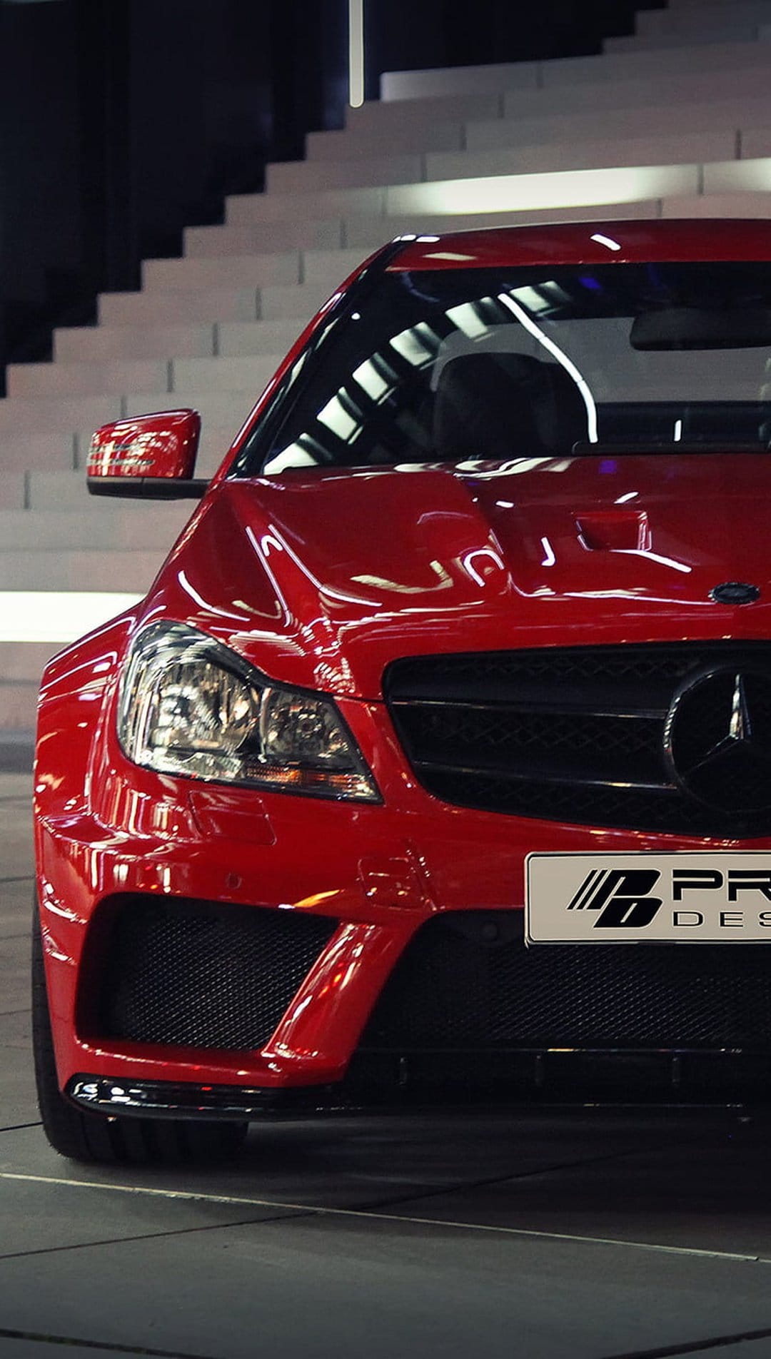 Red Mercedes-Benz C63 AMG with a custom BPP Design front bumper and grille parked near a modern staircase.