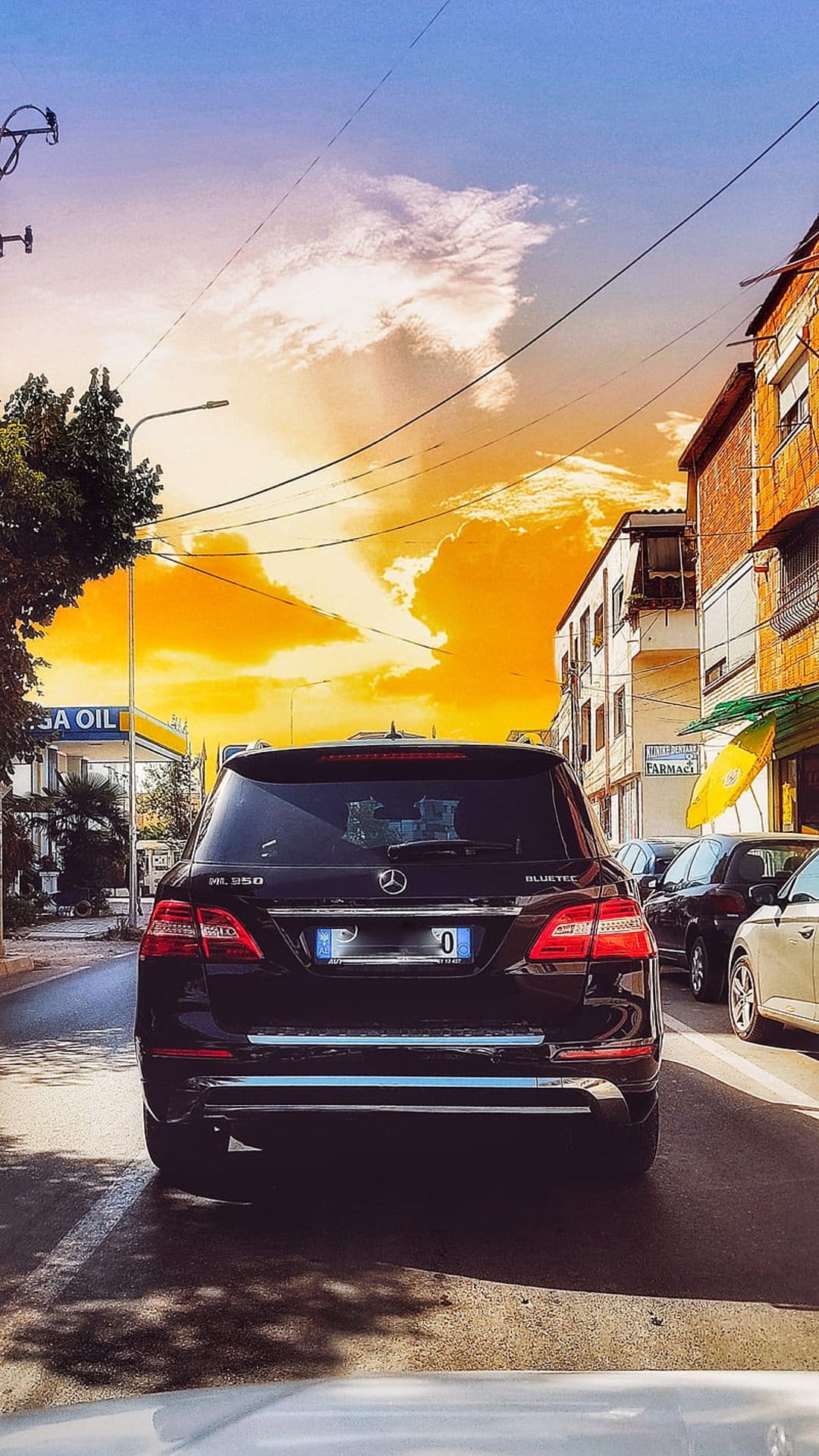 Mercedes ML 350 SUV driving on a city street toward a glowing orange sunset with dramatic clouds and power lines.