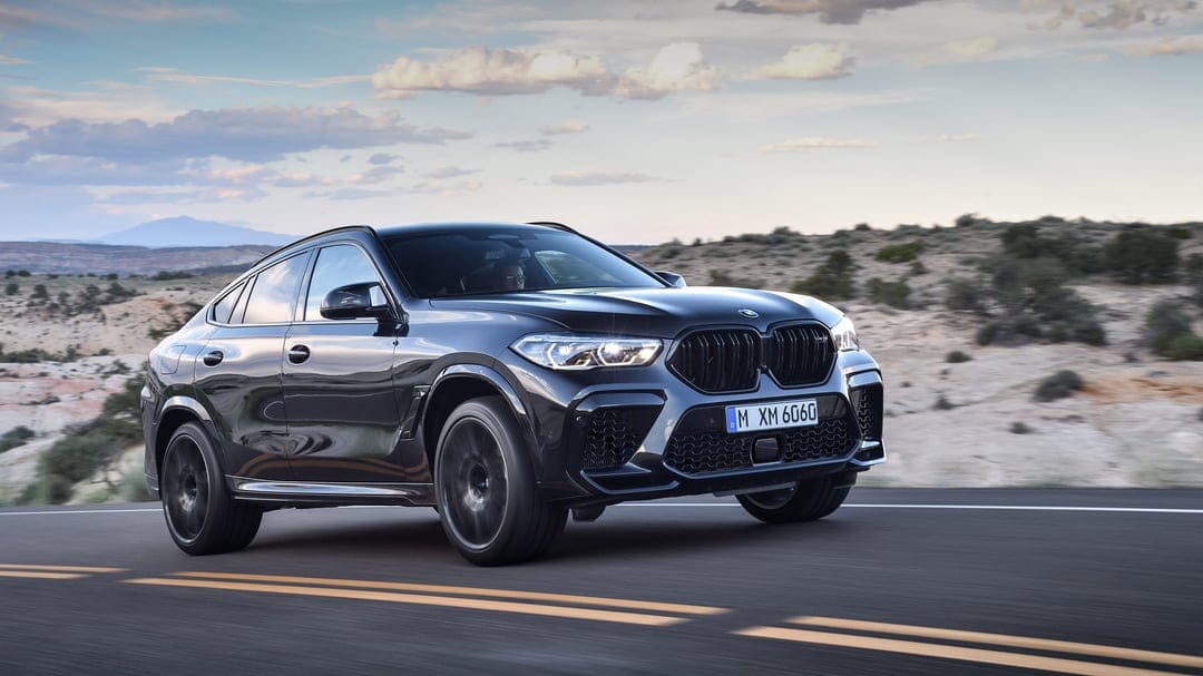 Black BMW X6 M Competition driving on a desert road with motion blur under a sunset sky during golden hour.