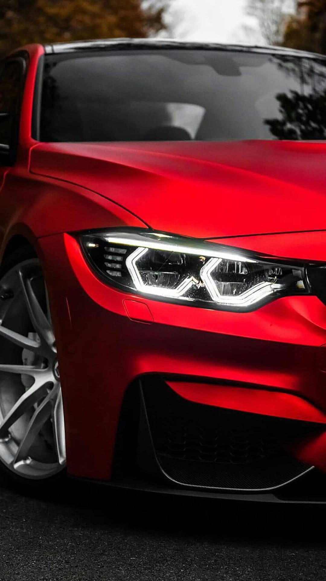 Red BMW M4 sports car features sharp LED headlights and dark multi-spoke wheels against a blurred green backdrop.