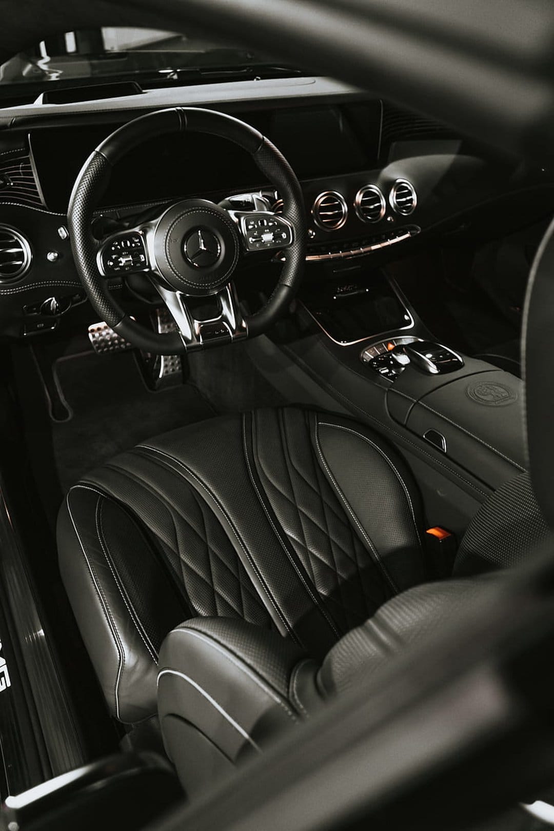Mercedes-Benz interior featuring black quilted leather seats, a chrome steering wheel, and illuminated vents.
