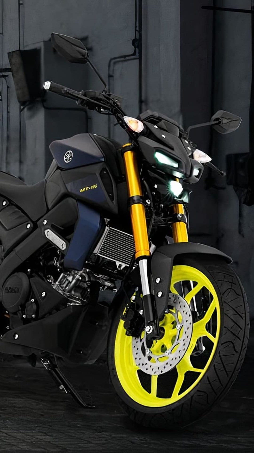 Yamaha MT-15 motorcycle with bright yellow forks and wheel rims parked in a dimly lit industrial setting.