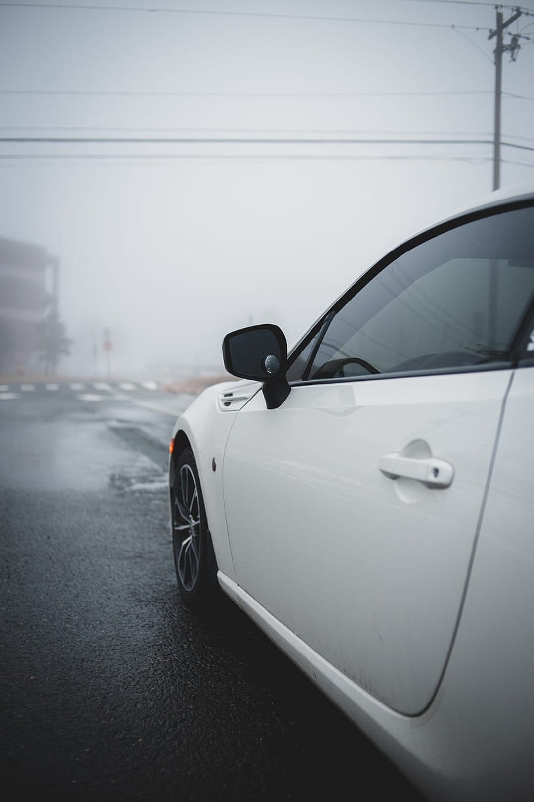 White sports car side profile on wet asphalt during a foggy night with a visible wheel and door handle.