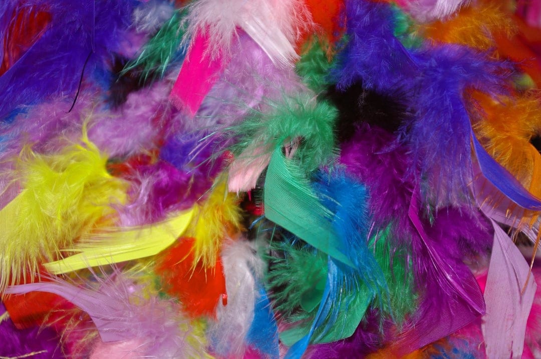 Brightly colored craft feathers in a dense pile showing soft textures of blue, pink, and yellow down plumes.
