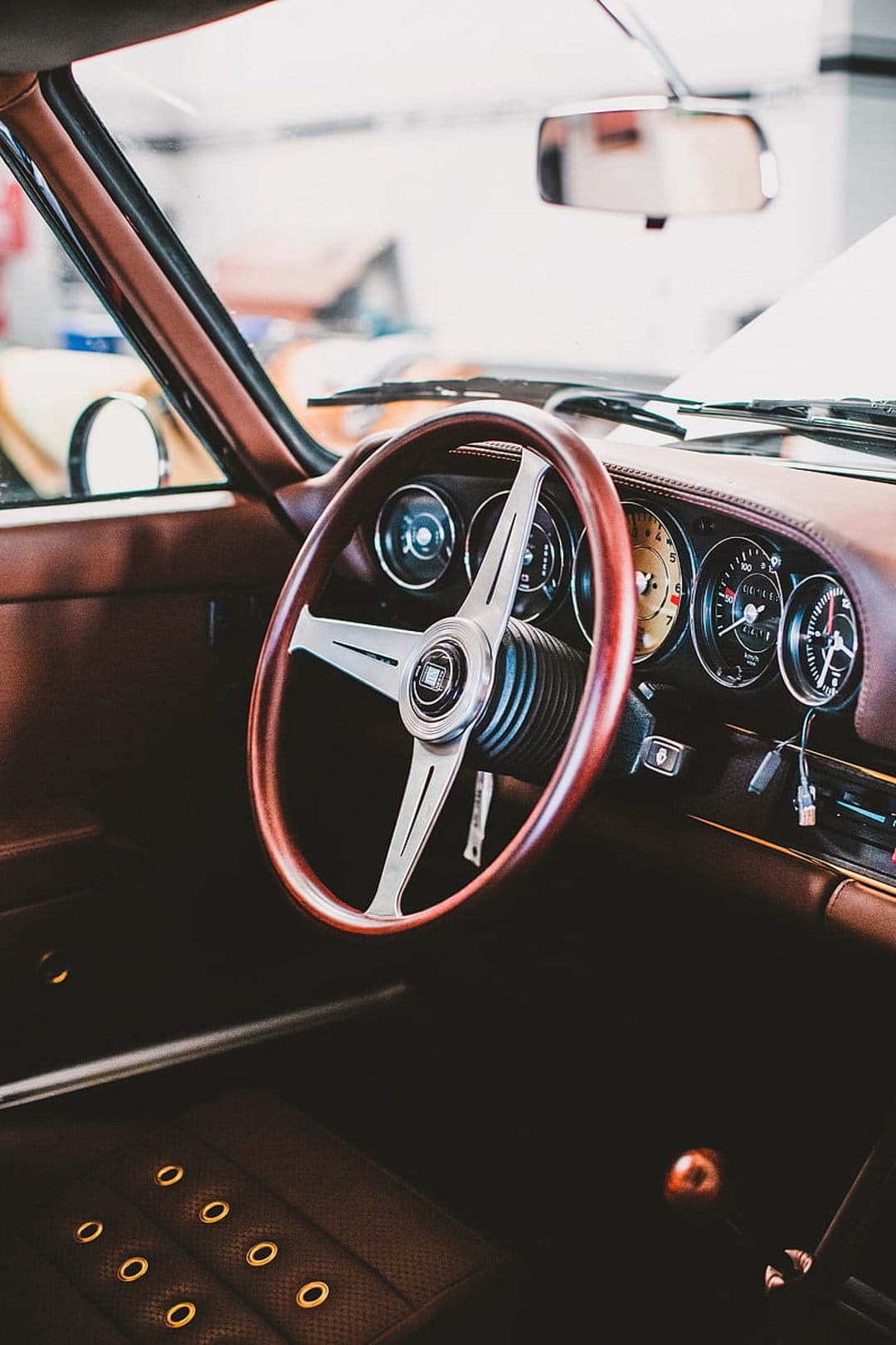 Polished mahogany steering wheel and stitched leather dashboard featuring analog gauges in a classic car interior.