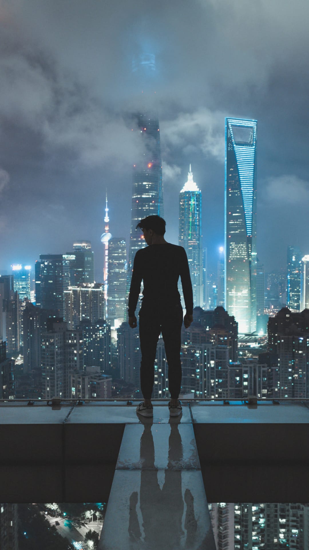 Person in silhouette stands on a skyscraper edge overlooking a blue-lit city with glowing skyscraper windows.