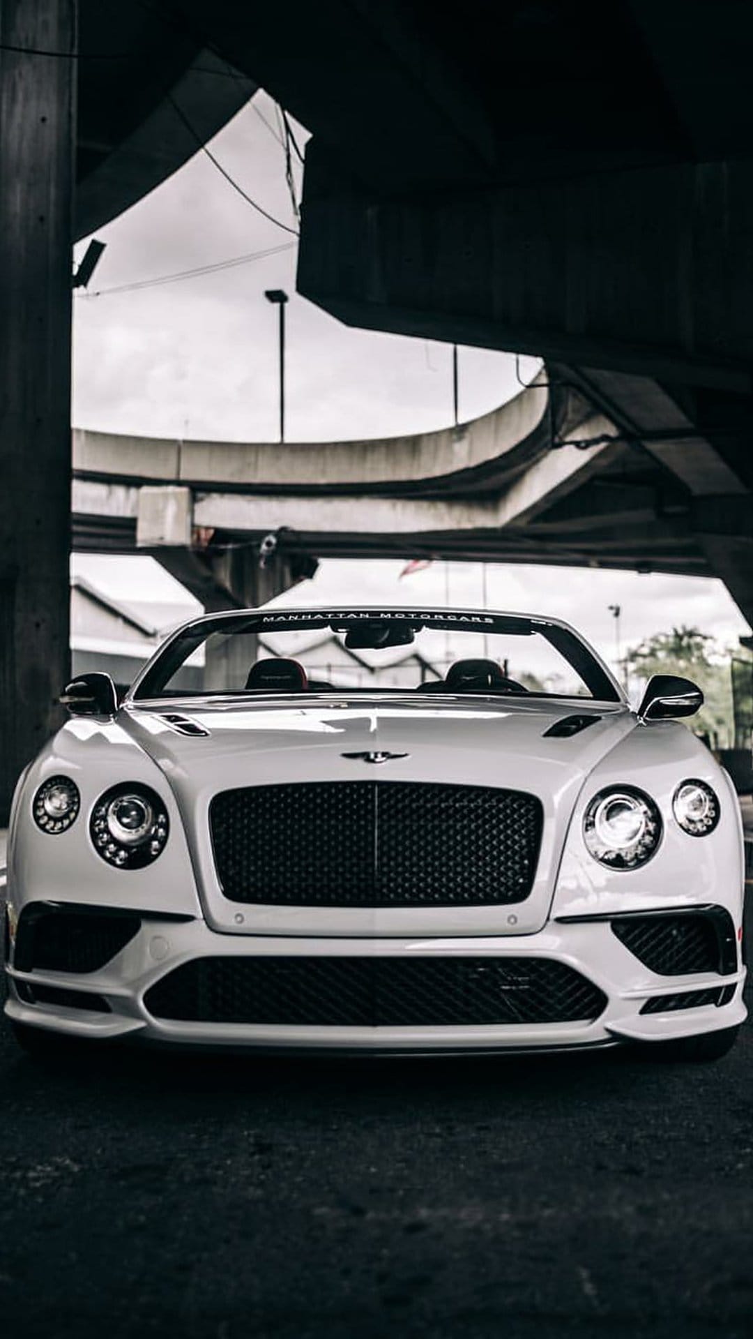White Bentley convertible with a classic grille parked under a concrete bridge with dramatic urban shadow lighting.