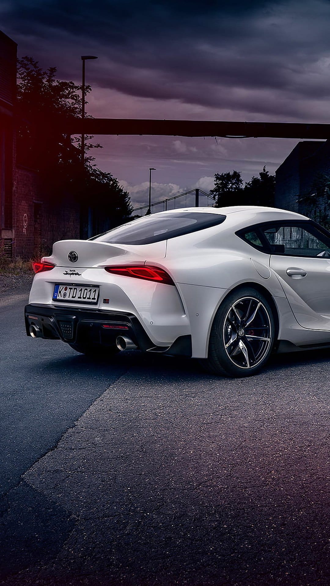 White Toyota Supra rear view parked on an asphalt road under a dark overcast sky with visible red taillights.