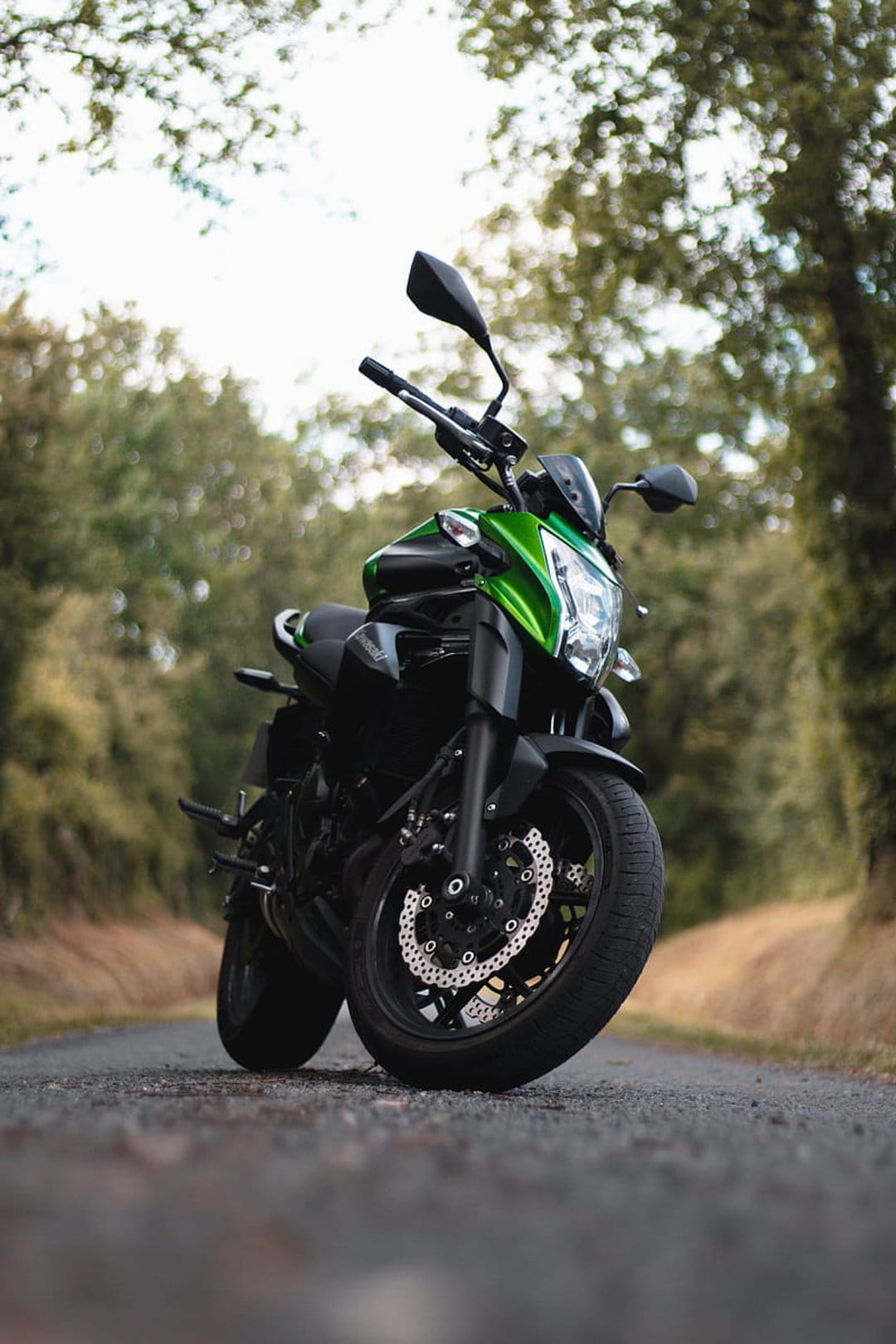 Green and black sport motorcycle parked on a gravel forest road with sunlight filtering through lush trees.