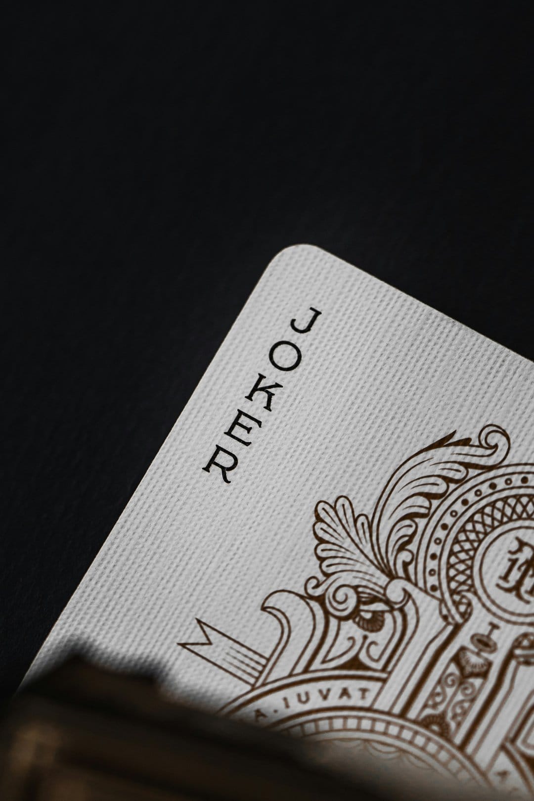 Joker playing card with intricate brown patterns angled against a textured black background in a macro shot.