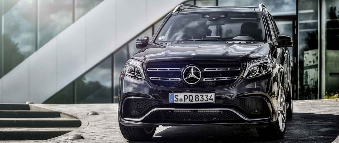 Black Mercedes-Benz GLS 63 AMG with a chrome grille parked in front of a modern glass and concrete building.