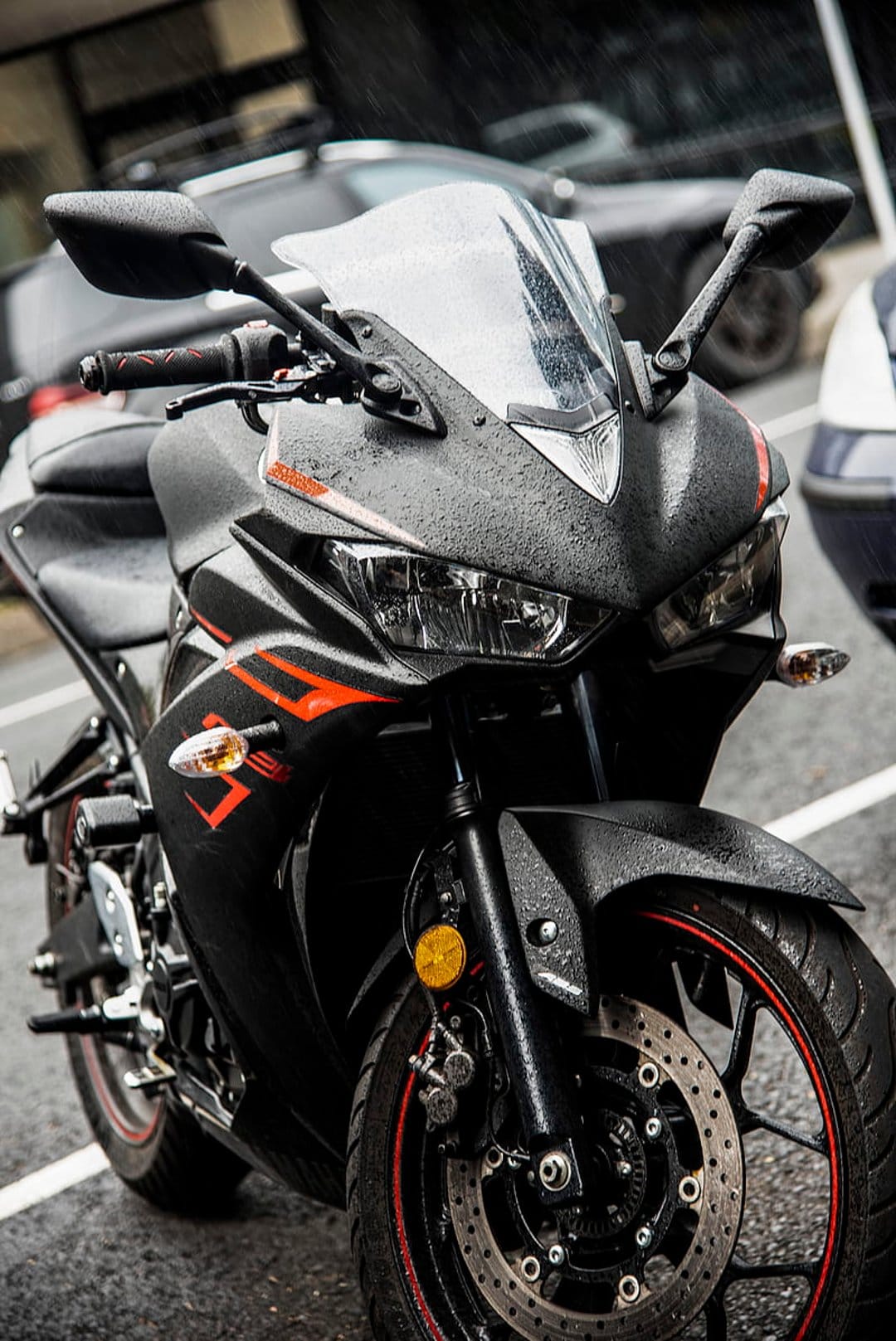 Black sportbike with red trim covered in rain droplets on a wet road during a dark atmospheric rainy day.