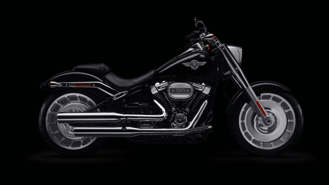 Side profile of a black Harley-Davidson Fat Boy 114 motorcycle with chrome accents on a dark background.