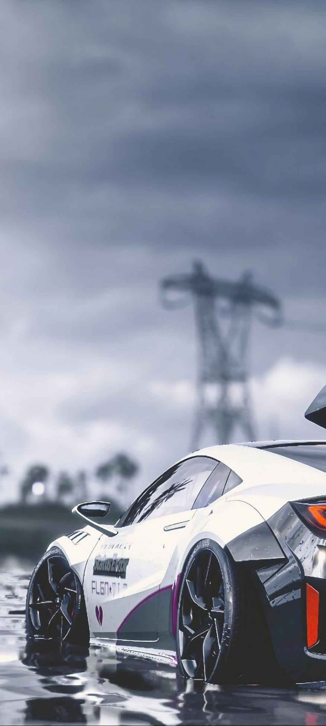 White sports car with a wide body kit sits on wet asphalt under a dark sky near a large electricity pylon.