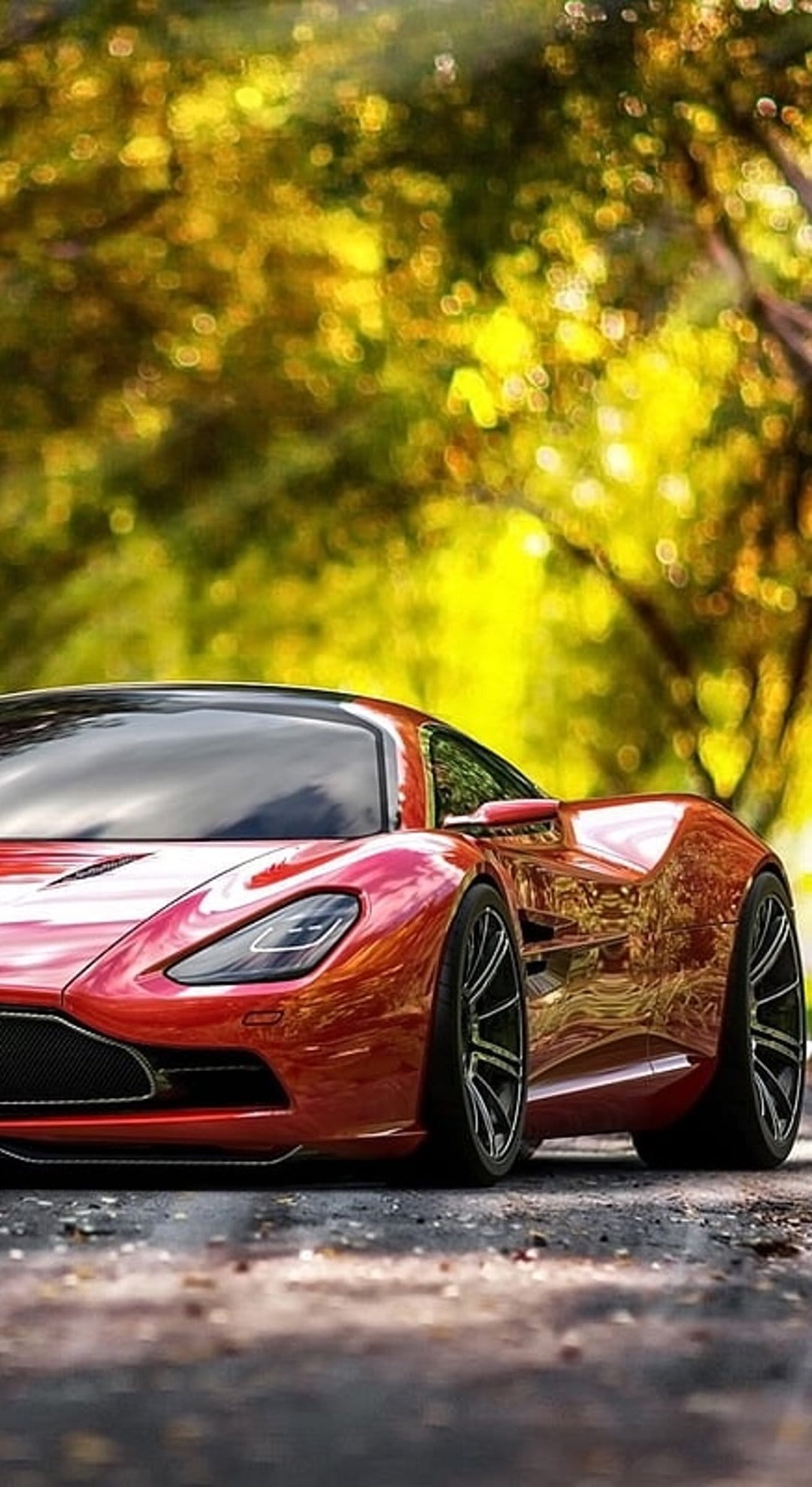 Red Aston Martin sports car parked on an asphalt road with blurred yellow autumn leaves in the background.