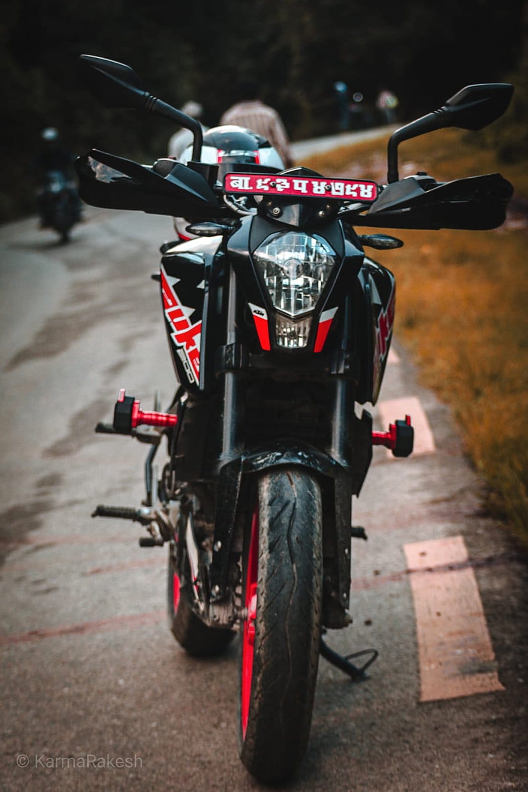 KTM Duke motorcycle with red wheels and frame parked on an asphalt road surrounded by blurred forest greenery.