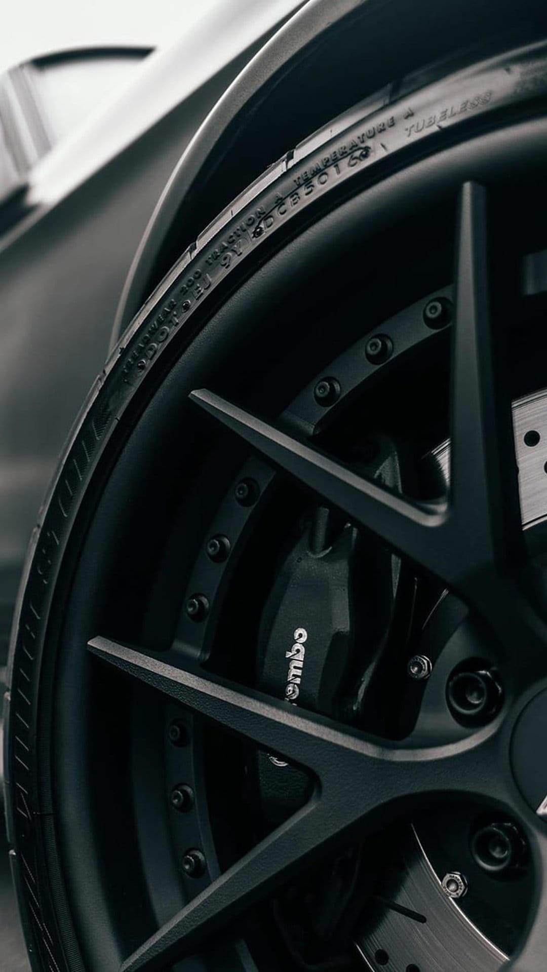 Black matte multi-spoke sports car wheel with a red Brembo brake caliper and detailed tire sidewall markings.