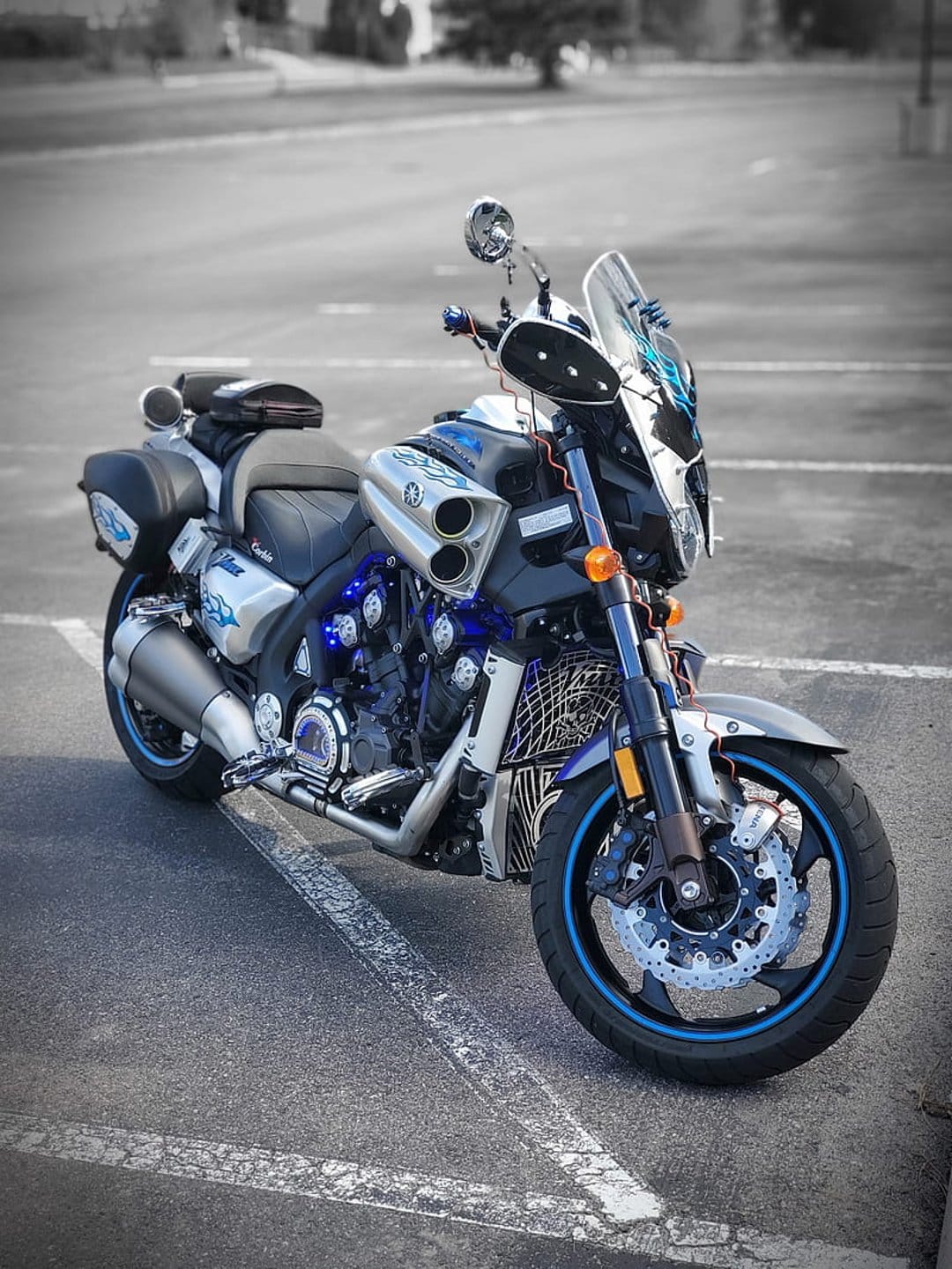 Silver Yamaha V-Max motorcycle with blue neon accents and dual exhaust pipes parked on a dark asphalt surface.