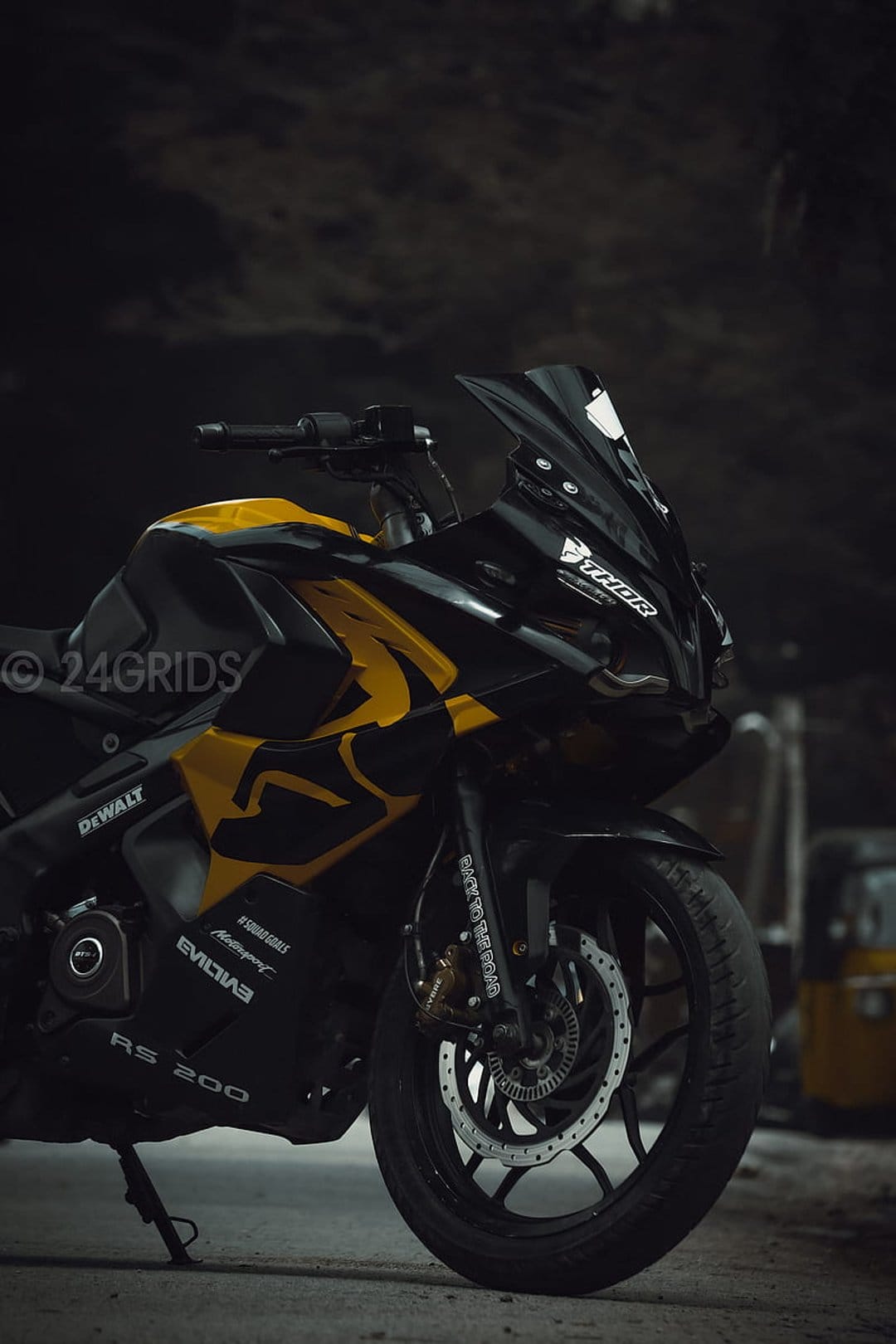 Black and yellow Pulsar RS 200 sportbike with a racing windshield and front wheel against a dark background.