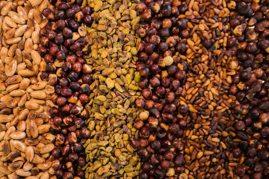 Almonds, coffee beans, green pistachios, and sunflower seeds arranged in vertical sections from a top-down view.