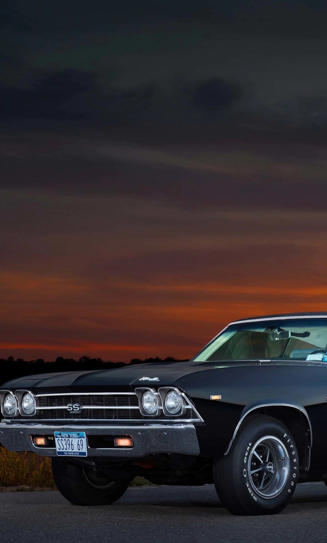 1969 Chevrolet Chevelle SS 396 muscle car parked against a fiery sunset with orange and dark indigo clouds.