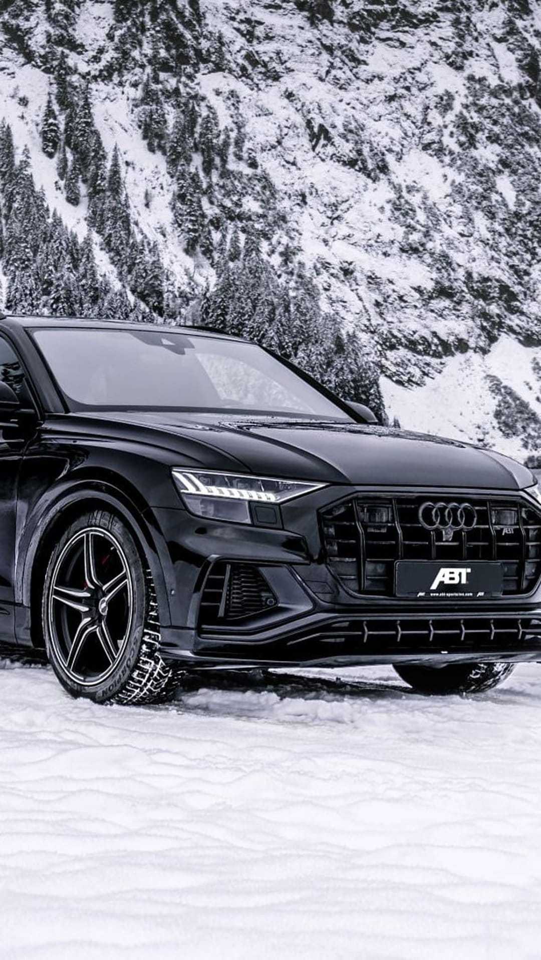 Black Audi RS Q8 ABT parked on a snowy mountain road with frosted pine trees and jagged peaks in the background.