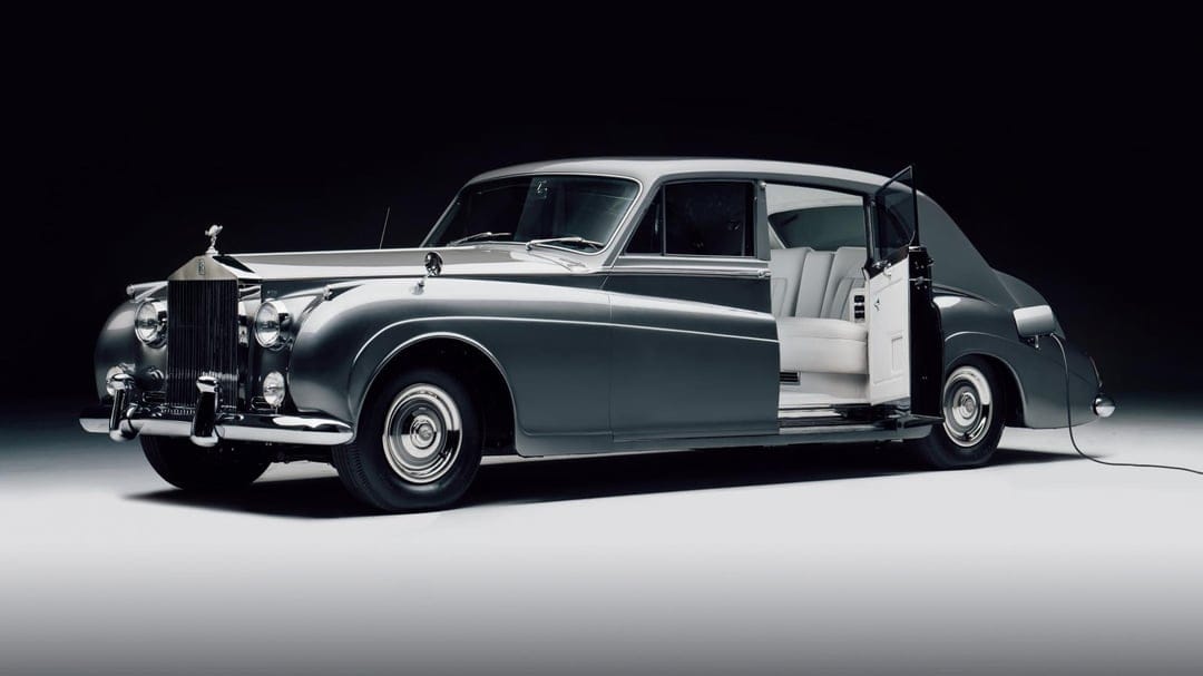 Silver vintage Rolls-Royce with an open rear door and white leather interior in a dark professional studio.