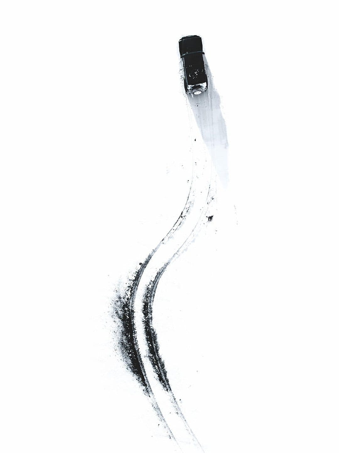 Black sports car drifting on a white surface leaving dark skid marks and smoke trails in a top-down view.