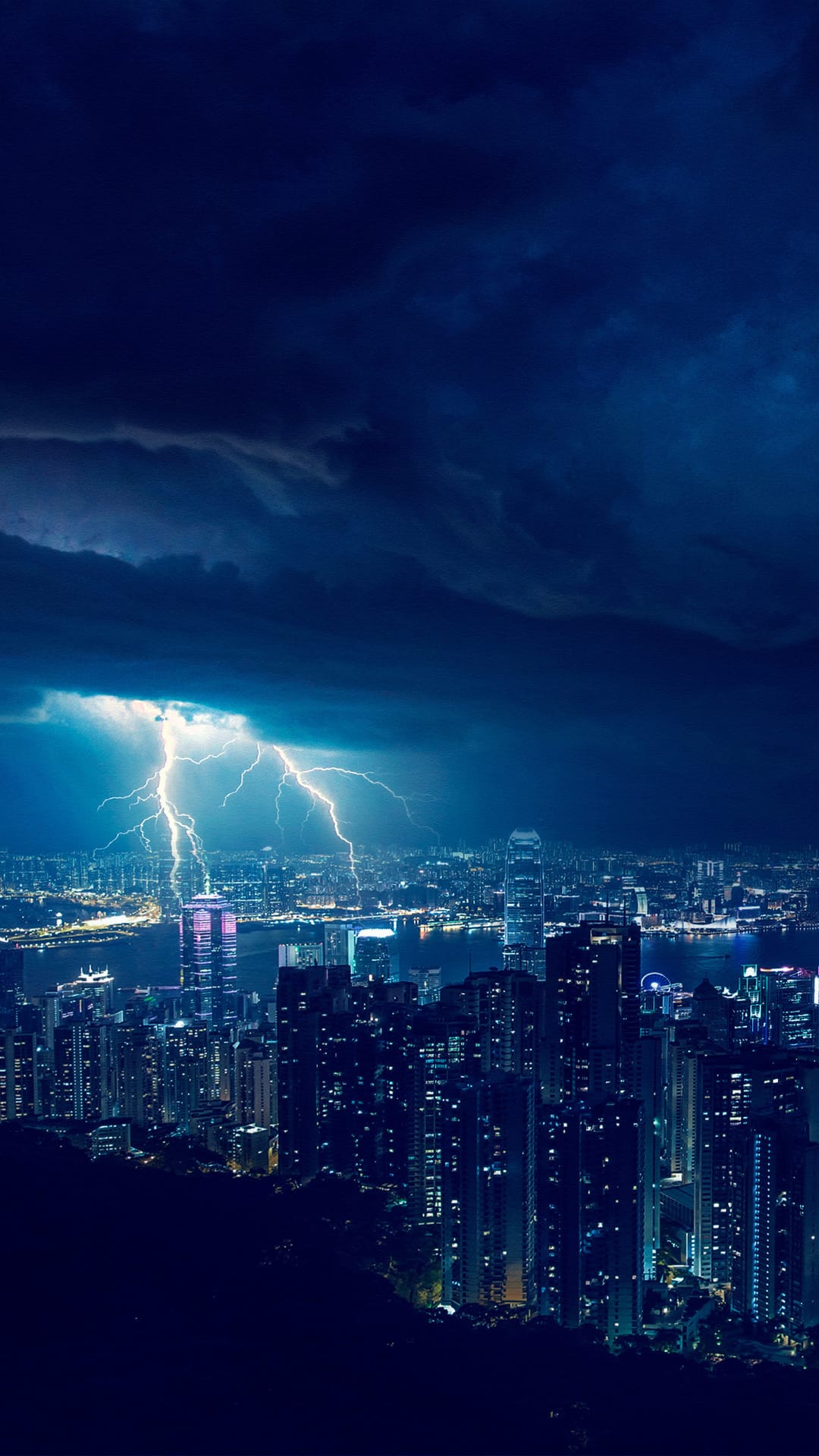 Vertical lightning bolts flash over a luminous metropolitan skyline and dark coastal waters at night.