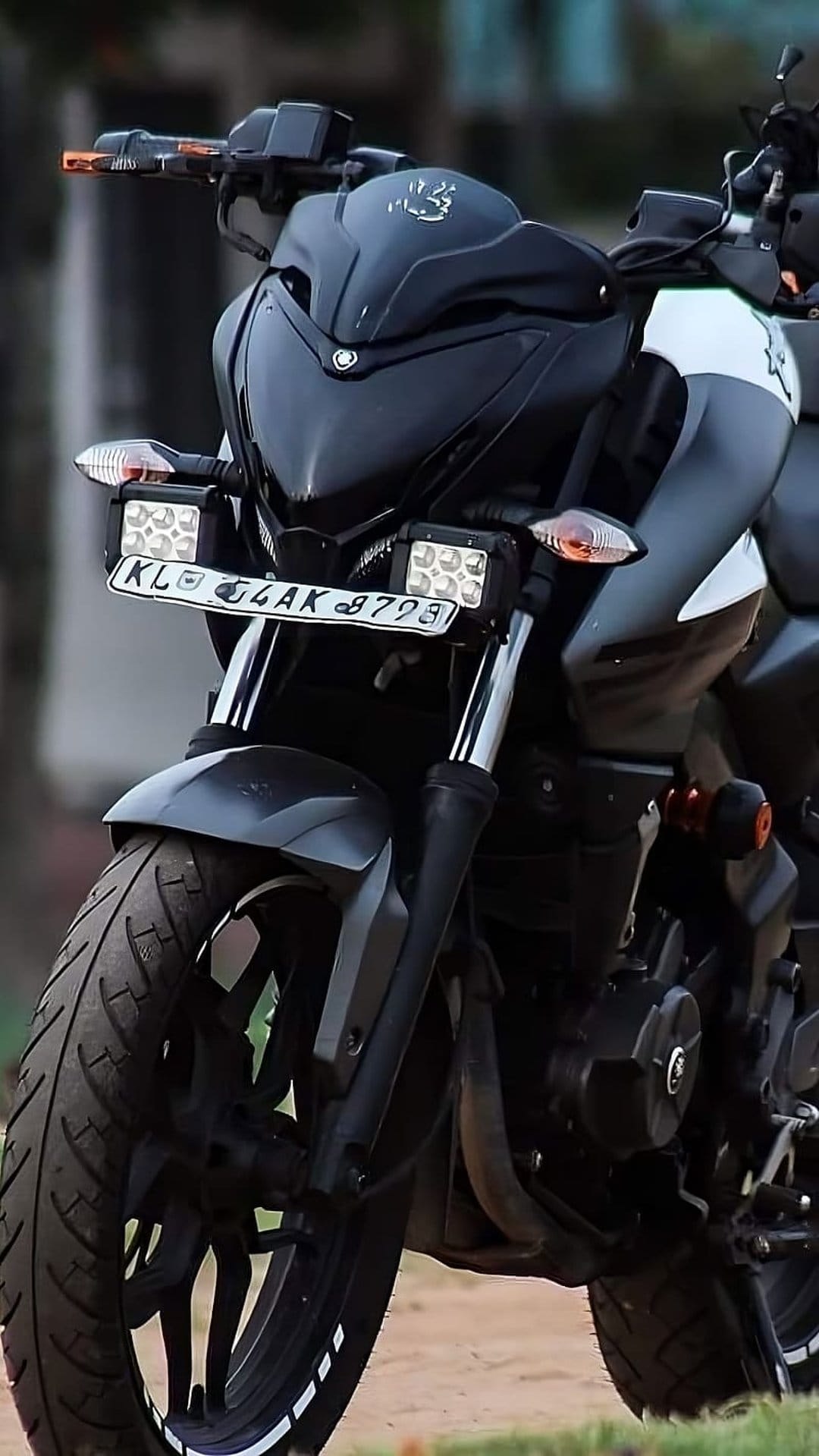 Bajaj Pulsar NS200 motorcycle with dual LED auxiliary lights and white rim stickers on a black front wheel.