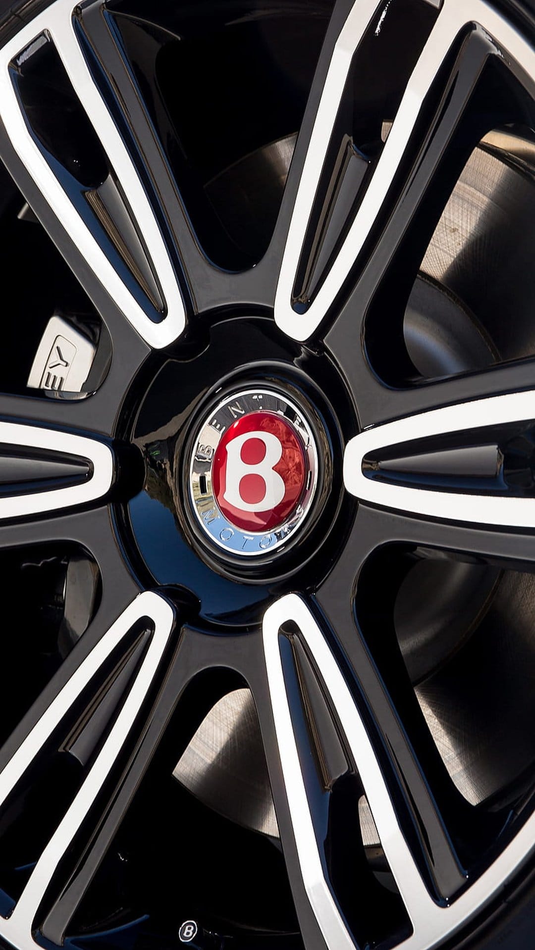 Bentley wheel center cap with a red and silver B logo on black alloy spokes and a visible metal brake disc.