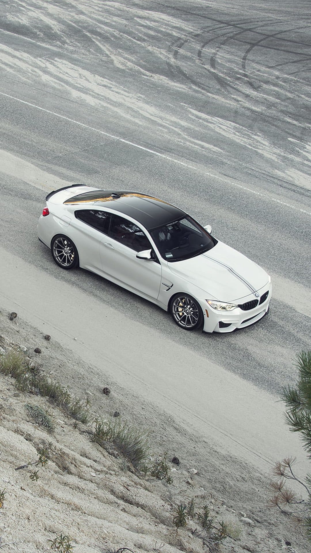 White BMW M4 coupe with racing stripes and a black roof parked on a dusty road with visible tire tracks.