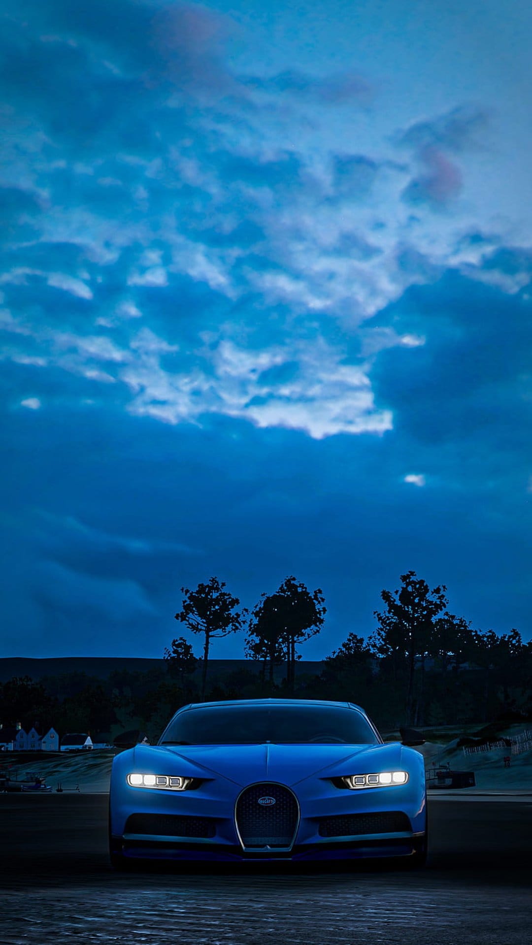 Blue Bugatti Chiron with glowing headlights parked on a dark road under a dramatic evening sky with clouds.