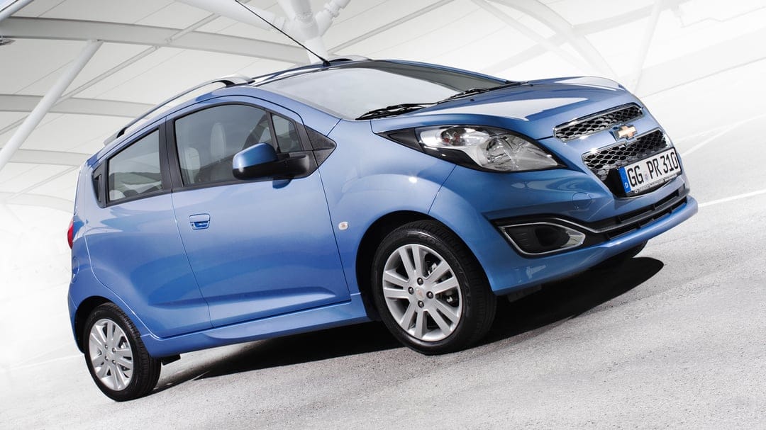 Blue compact car parked at an angle against a bright white architectural background with modern structures.